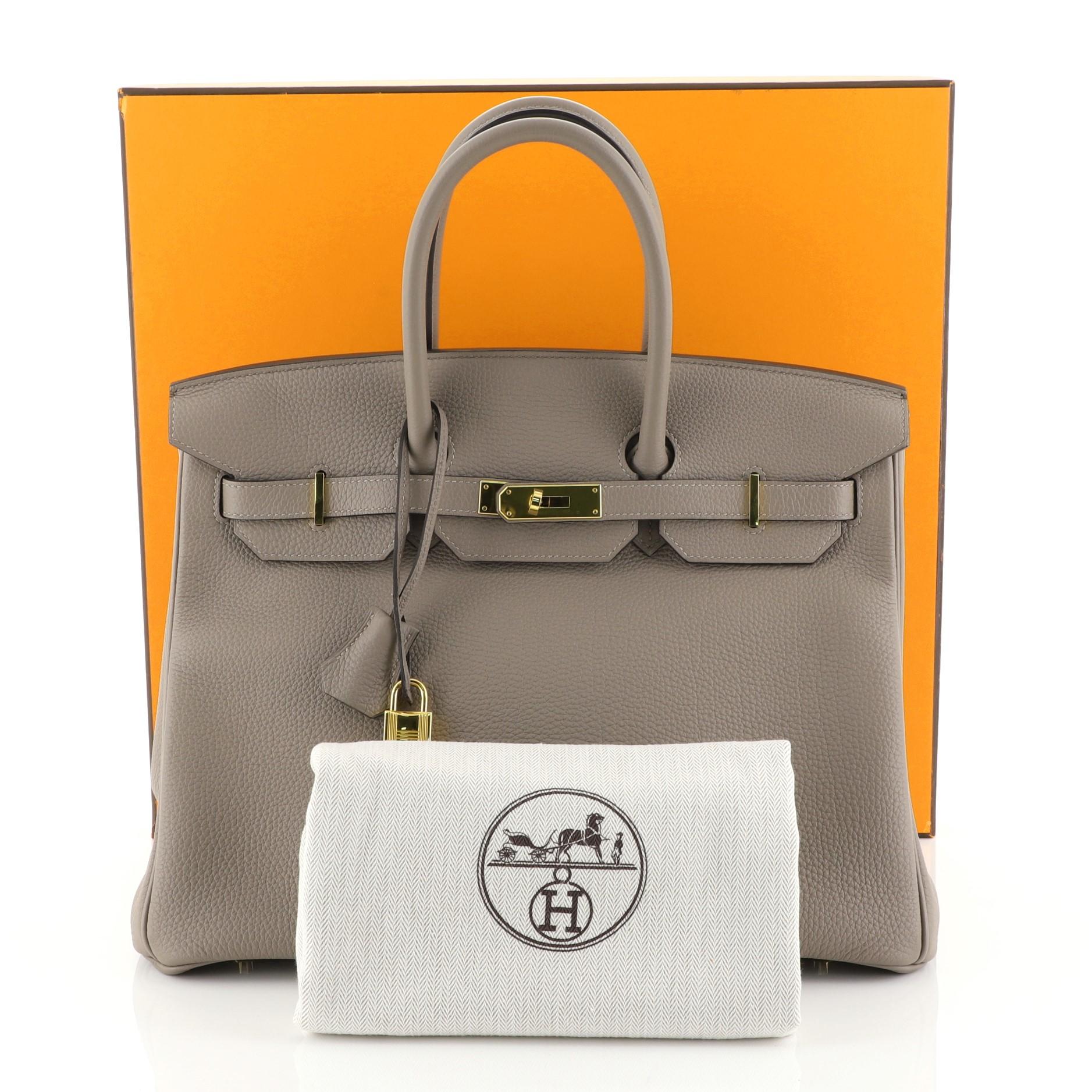 This Hermes Birkin Handbag Gris Asphalte Togo with Gold Hardware 35, crafted in Gris Asphalte grey Togo leather, features dual rolled handles, frontal flap, and gold hardware. Its turn-lock closure opens to a Gris Asphalte grey Chevre leather