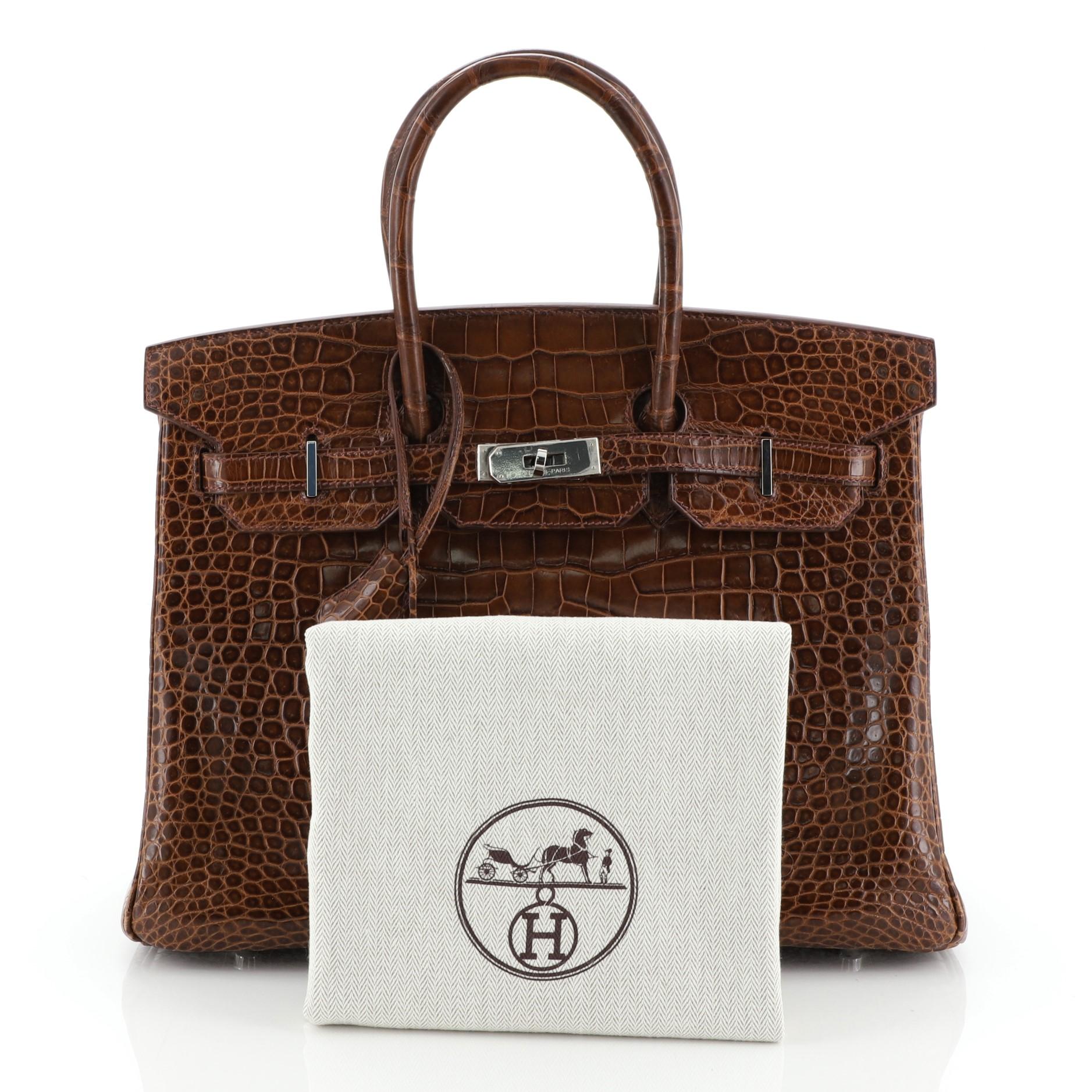 This Hermes Birkin Handbag Miel Shiny Porosus Crocodile with Palladium Hardware 35, crafted in genuine Miel brown Shiny Porosus Crocodile, features dual rolled handles, frontal flap, and palladium hardware. Its turn-lock closure opens to a Miel