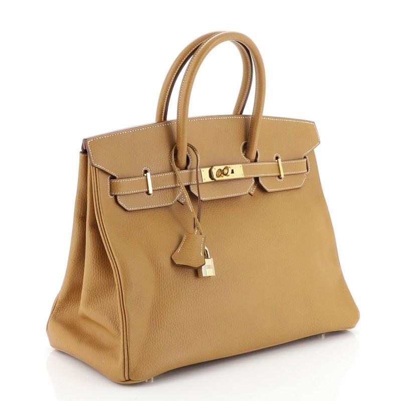 This Hermes Birkin Handbag Natural Ardennes with Gold Hardware 35, crafted in Natural brown Ardennes leather, this handbag features dual rolled top handles, frontal flap, and gold hardware. Its turn-lock closure opens to a Natural brown Chevre