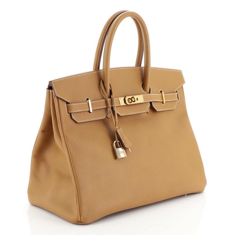 This Hermes Birkin Handbag Natural Ardennes with Gold Hardware 35, crafted in Natural brown Ardennes leather, features dual rolled handles, frontal flap, and gold hardware. Its turn-lock closure opens to a Natural brown Chevre leather interior with