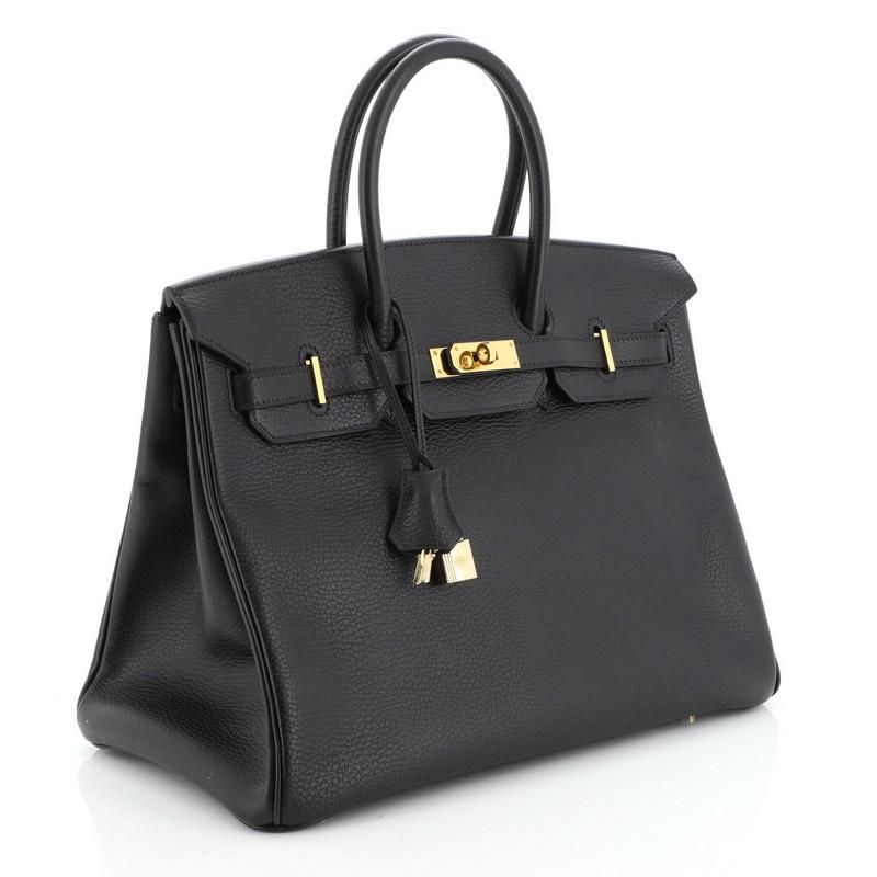 This Hermes Birkin Handbag Noir Ardennes with Gold Hardware 35, crafted in Noir black Ardennes leather, features dual rolled top handles, frontal flap, and gold-tone hardware. Its turn-lock closure opens to a black leather interior with side zip and