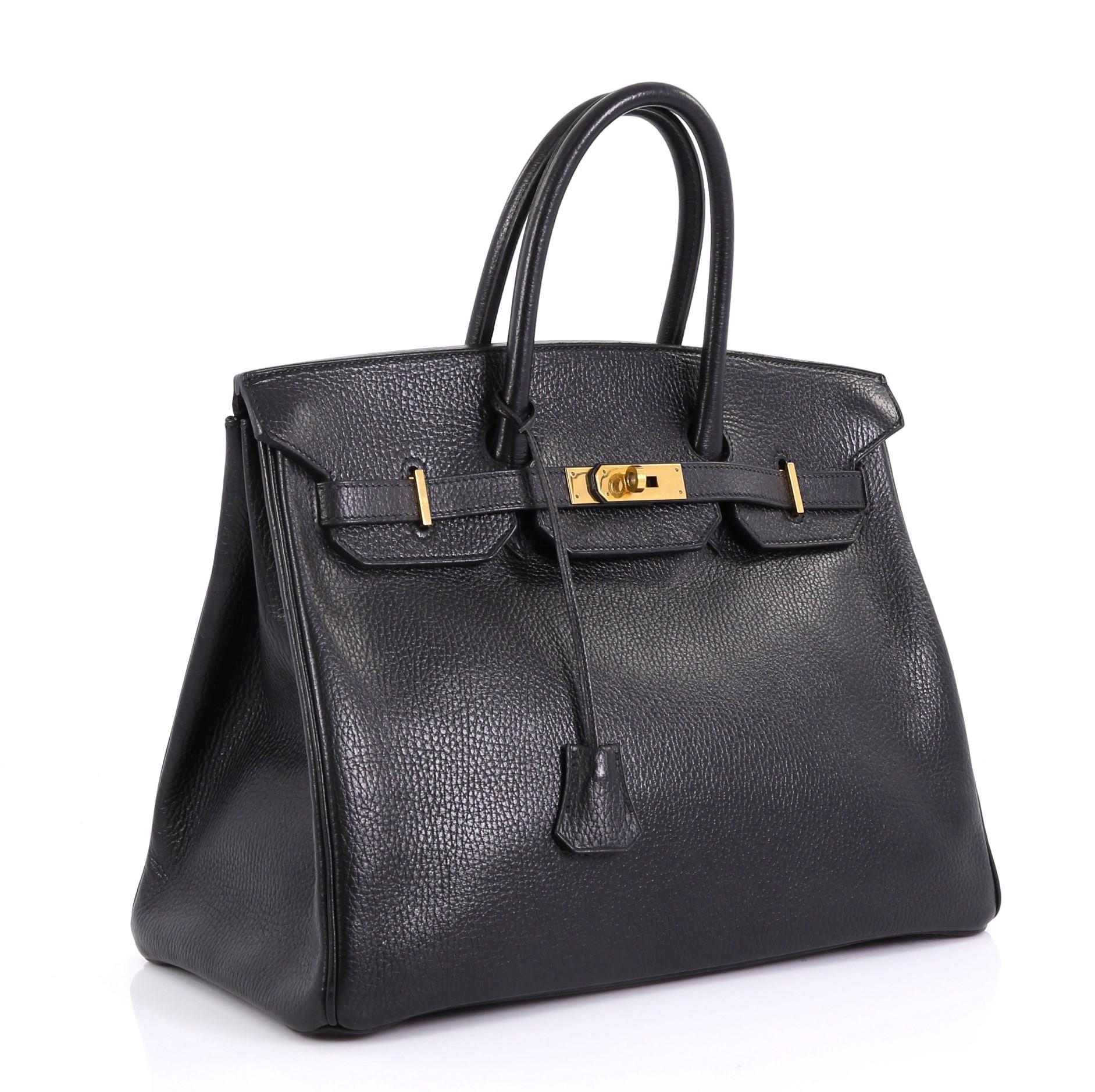 This Hermes Birkin Handbag Noir Ardennes with Gold Hardware 35, crafted in Noir black Ardennes leather, features dual rolled handles, frontal flap, and gold hardware. Its turn-lock closure opens to a Noir black Chevre leather interior with slip