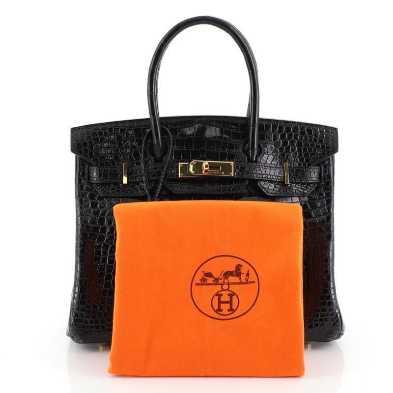 This Hermes Birkin Handbag Noir Shiny Porosus Crocodile with Gold Hardware 30, crafted in genuine Noir black Shiny Porosus Crocodile, features dual rolled handles, frontal flap, and gold hardware. Its turn-lock closure opens to a Noir black leather