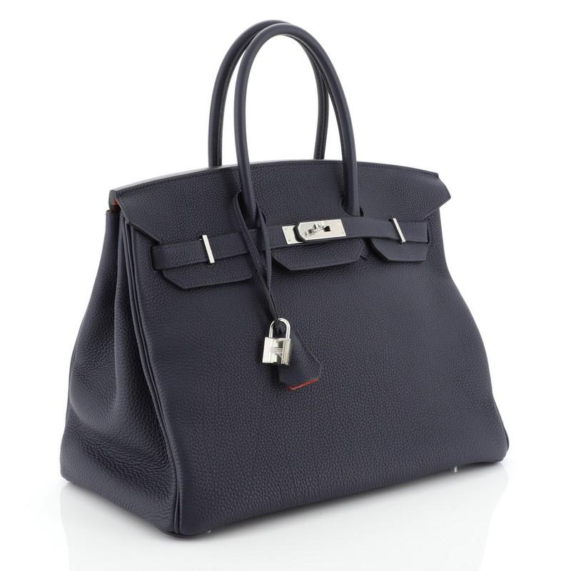 This Hermes Birkin Handbag Verso Togo with Palladium Hardware 35, crafted in Bleu Nuit blue Togo leather, features dual rolled top handles, frontal flap, and palladium hardware. Its turn-lock closure opens to an Orange Poppy orange Chevre leather