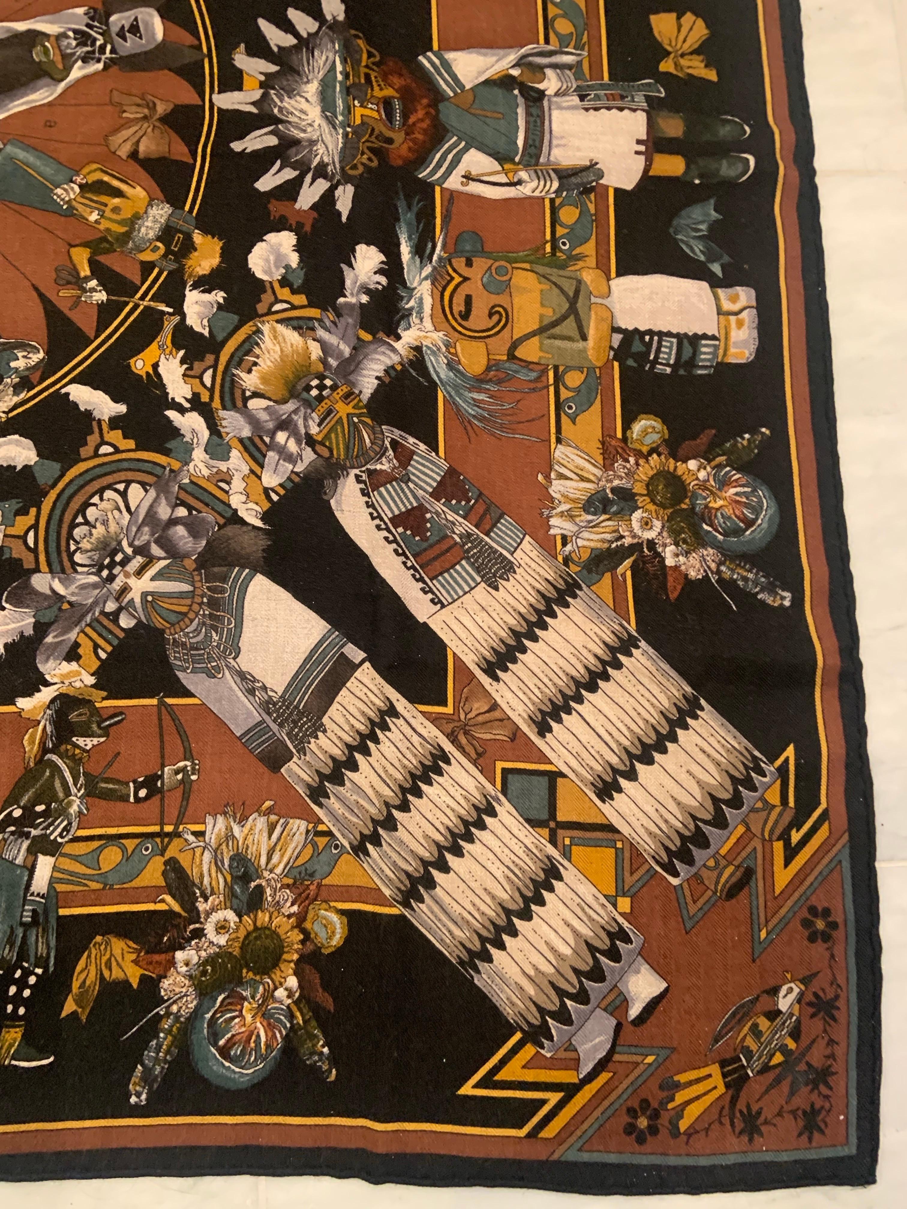 Inspirée de la culture amérindienne du Sud-Ouest, cette écharpe en soie Kachina se décline en noir, marron, gris moutarde et bleu profond dans un mélange de cachemire et de soie.  Le dessin montre des Kachinas participant à diverses cérémonies.