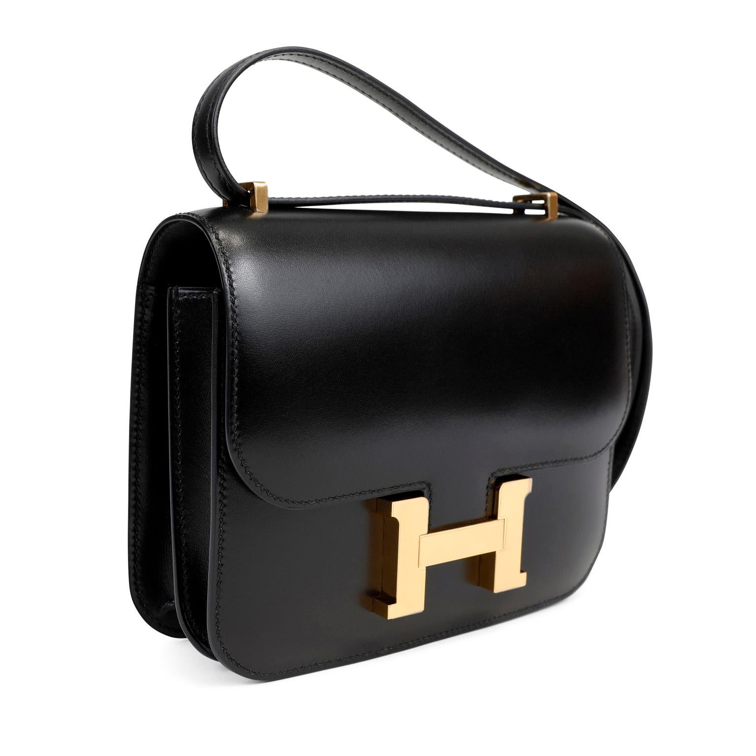 This authentic Hermès Black Box Calf Mini Constance in pristine condition.  The Constance has simple clean lines and combines classic with modern.  The adjustable strap allows for shoulder or cross body wear. The large gold tone signature Hermès