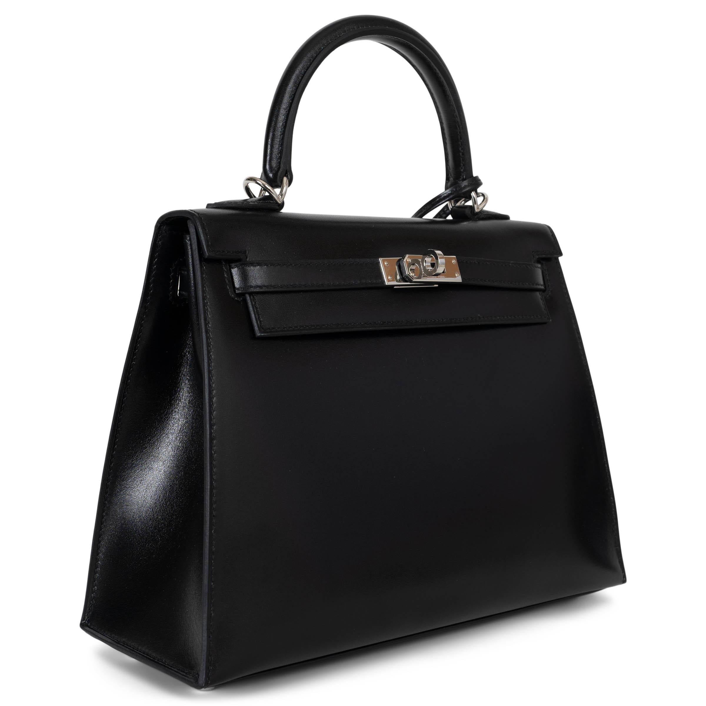 Este bolso Hermès Kelly 25 Sellier 100% auténtico en piel Noir (negra) Veau Box es una auténtica pieza de coleccionista, fabricada con una de las pieles más codiciadas y raras de Hermès. La piel de Veau Box es apreciada por su acabado liso y