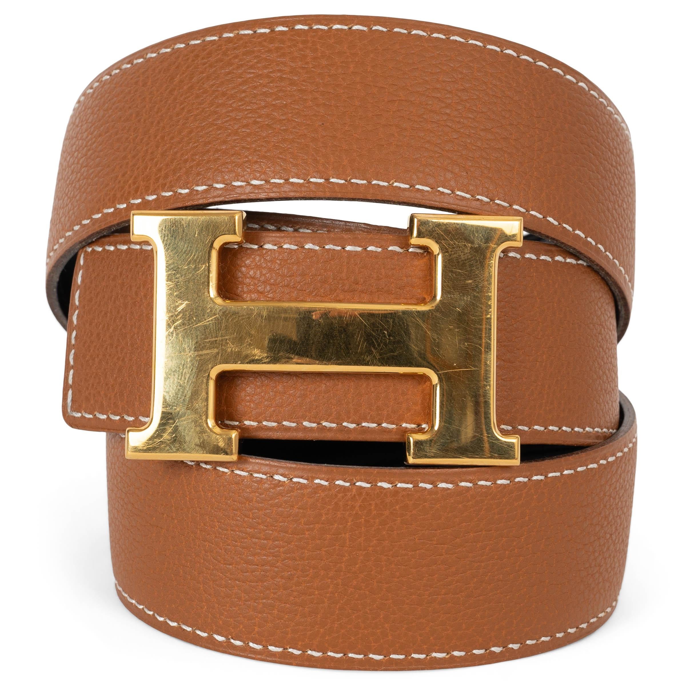 Questa cintura reversibile da 32 mm, autentica al 100%, è un accessorio senza tempo realizzato in lussuosa pelle Veau Box nera da un lato e in pelle Veau Togo oro (cammello) dall'altro, che offre opzioni di stile versatili in un unico pezzo.