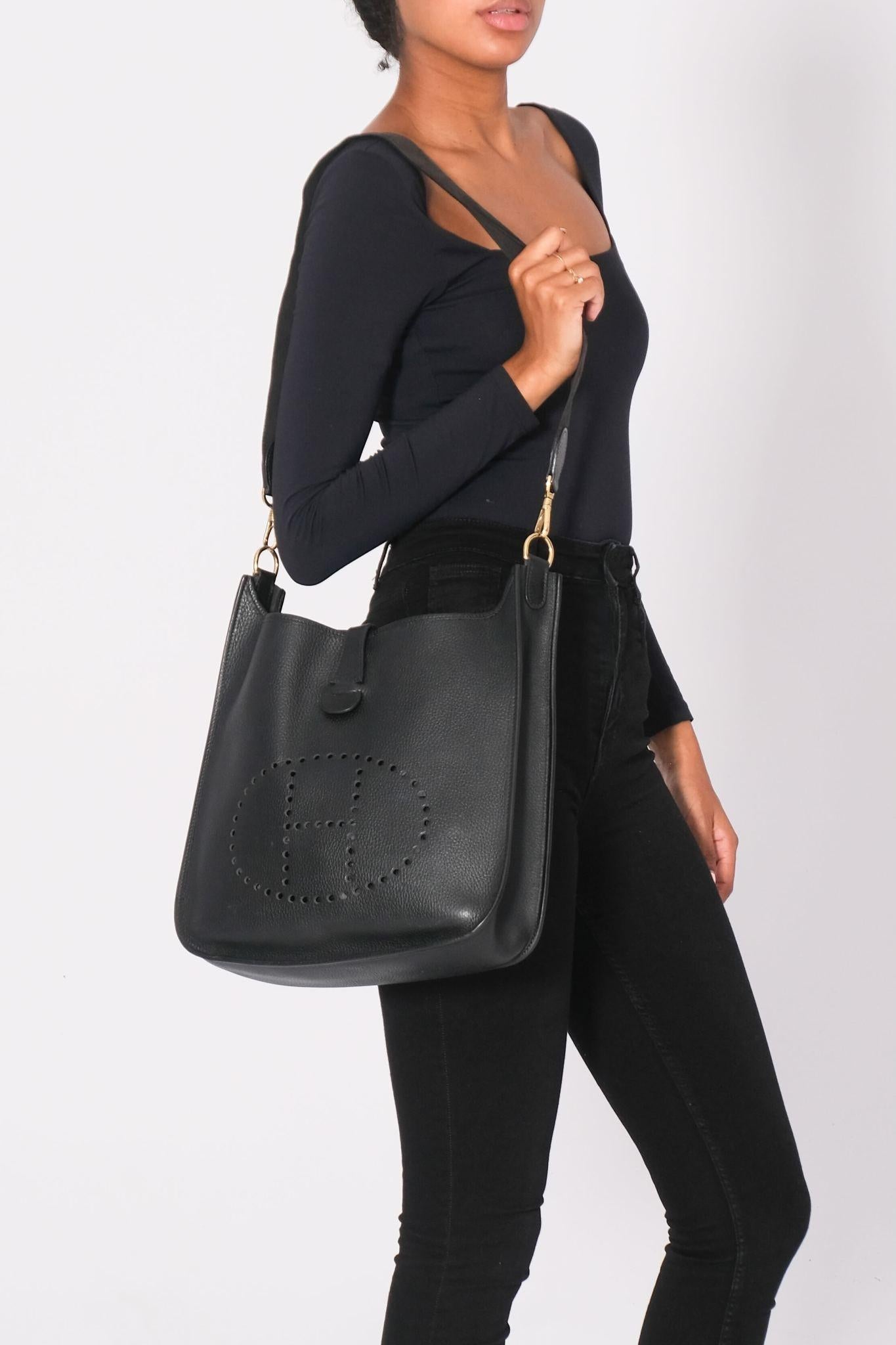 This bag is made of Ardennes leather in black. The shoulder bag features a canvas strap, a front perforated Hermes H, and light gold plated hardware including clasps for the shoulder strap. The bag has an open top and a matching suede interior. Gen