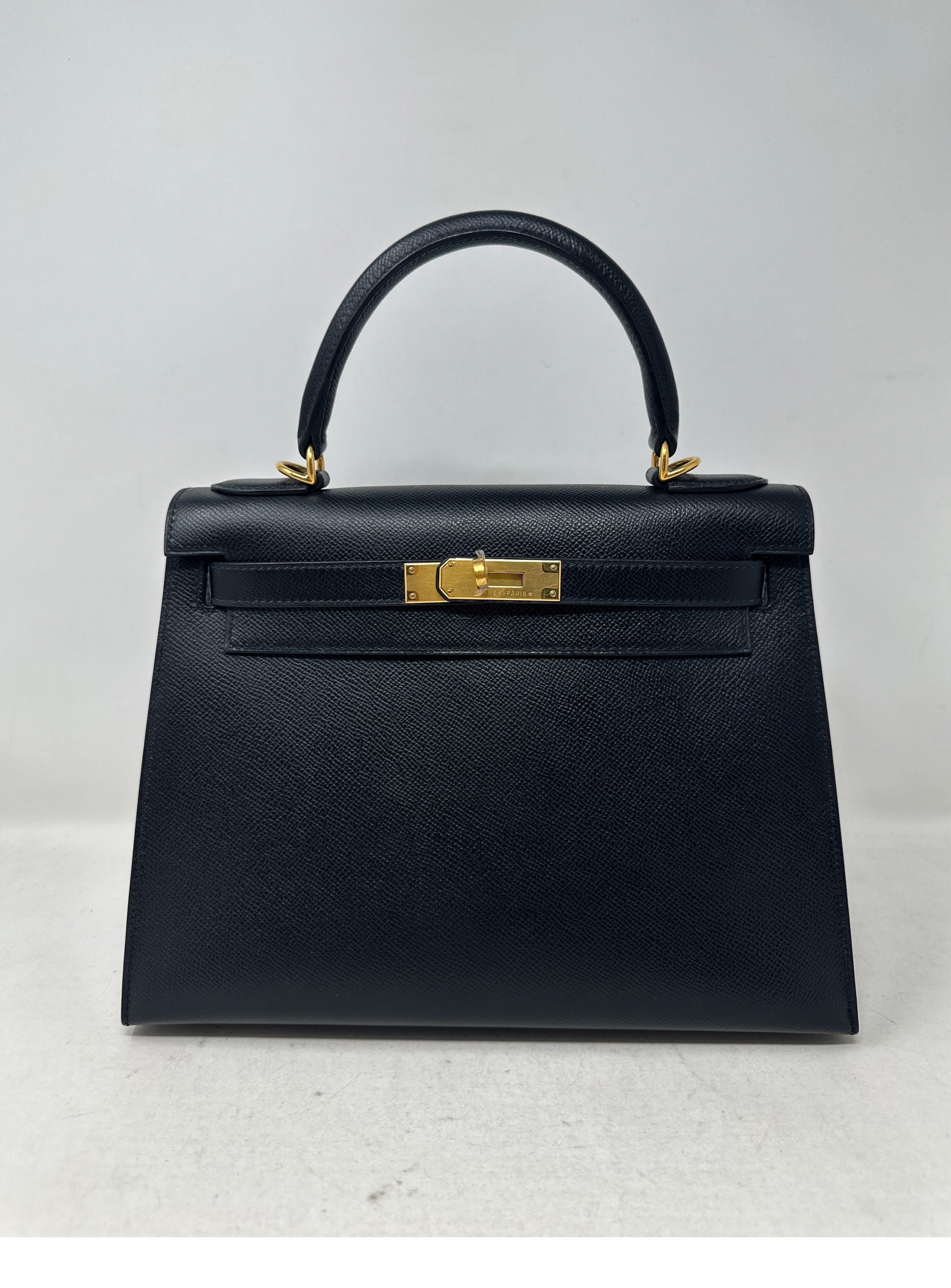 Sac Kelly 28 noir de Hermes. Elle semble neuve. Excellent état. Cuir d'epsom sellier noir. Matériel doré. Le plastique est toujours sur le matériel. Jamais utilisé. Comprend une clochette, un cadenas, des clés et un sac à poussière. Garantie