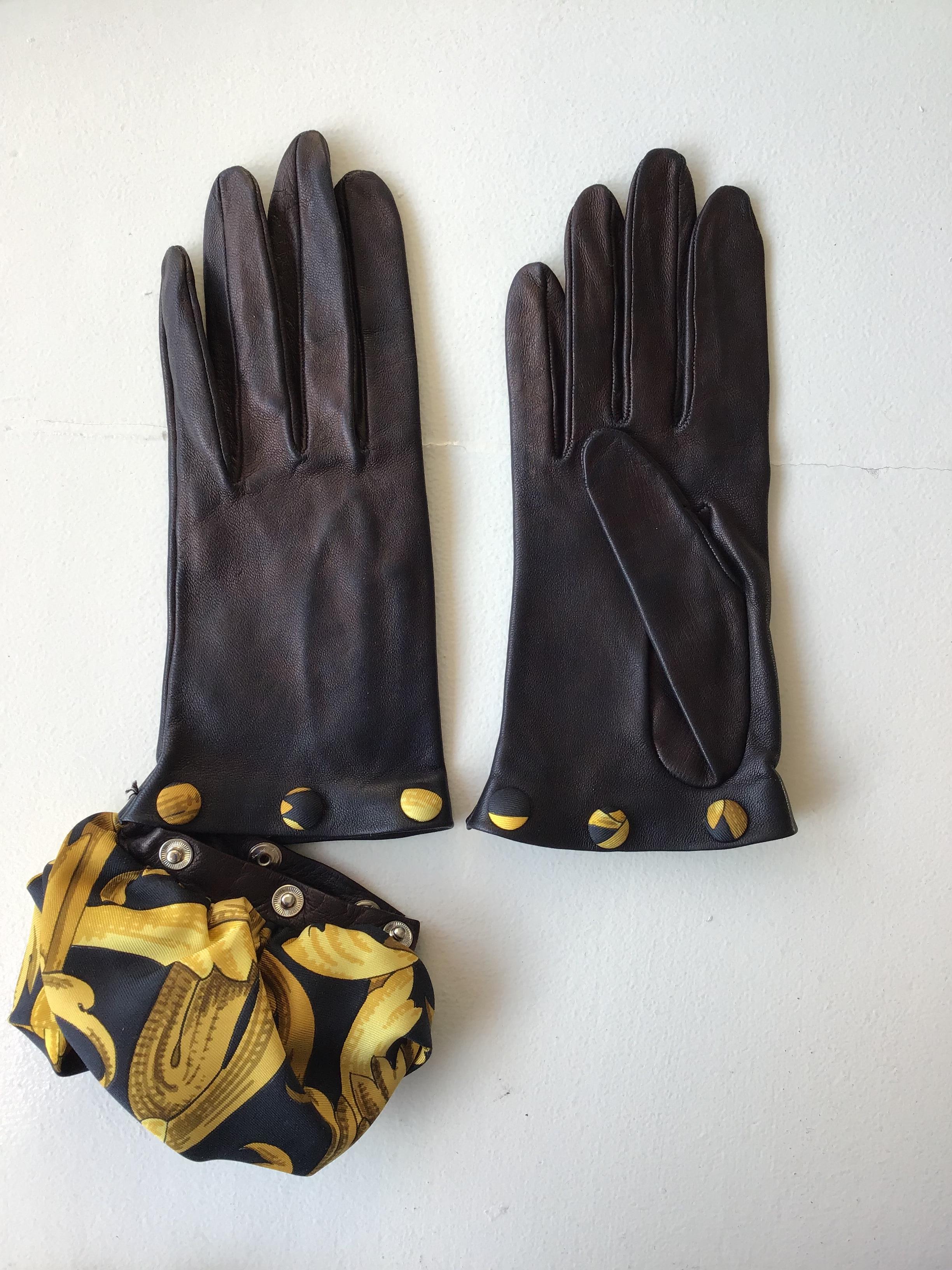 Hermes Black Leather Gloves with Optional Silk Cuffs. The gloves are composed of a calfskin leather, with suede interior, and a signature Hermes print cuff. The silk scarf cuff features a black background with gold accents in undulating, floral