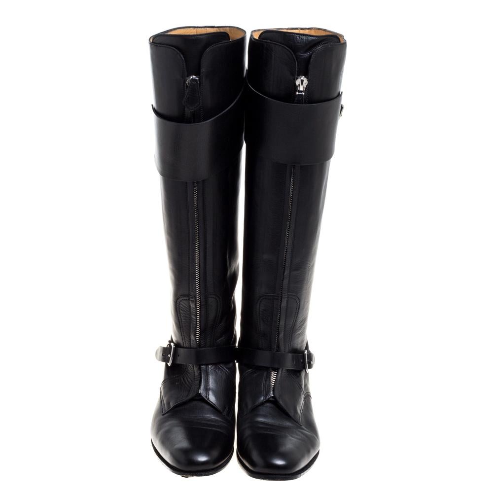 This bold yet chic pair of Hermes boots has a stylish silhouette and simple design. The knee-high boots have been crafted from black leather featuring chain detail on the front and buckled straps on the ankles and at the top. Representing the power