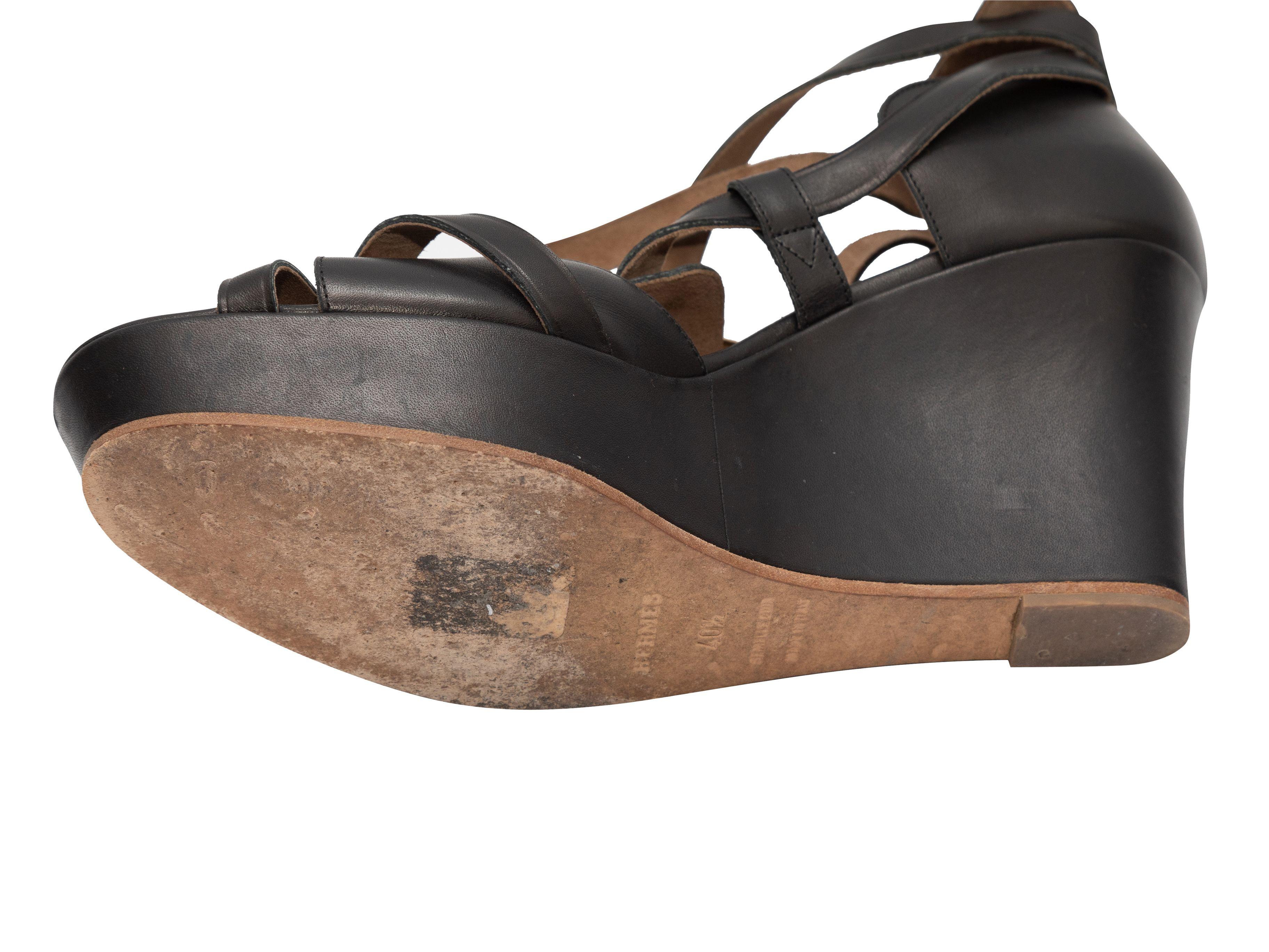 Détails du produit : Sandales compensées en cuir noir de la marque Hermès. Fermetures à boucle en métal doré au niveau de la cheville. Hauteur de la plateforme de 1,5