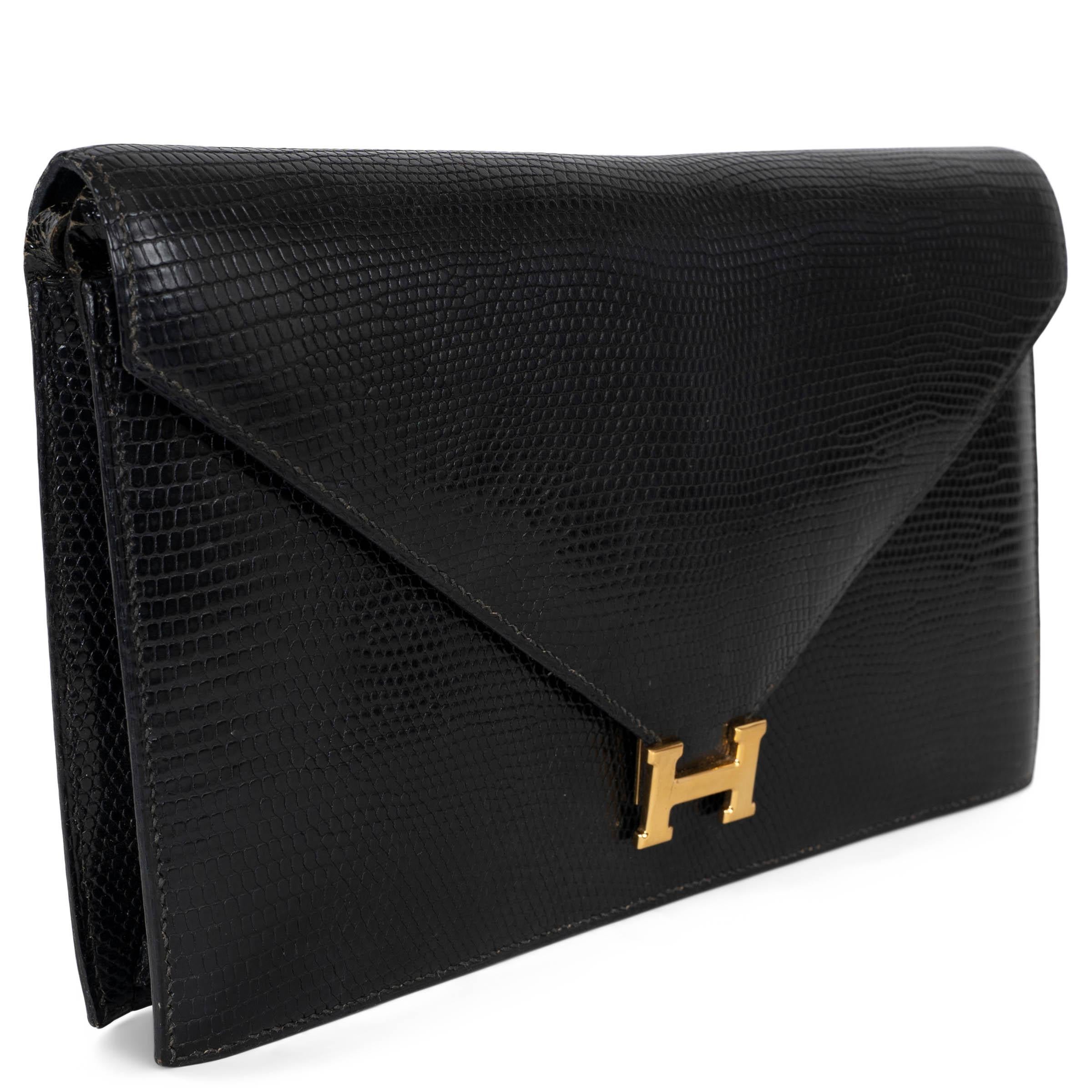 Cette pochette Lydie, 100% authentique, est réalisée en cuir de lézard noir et dotée d'un fermoir H doré sur le rabat en forme d'enveloppe. Il présente une silhouette fine et structurée, avec une bandoulière en cuir détachable pour un portage