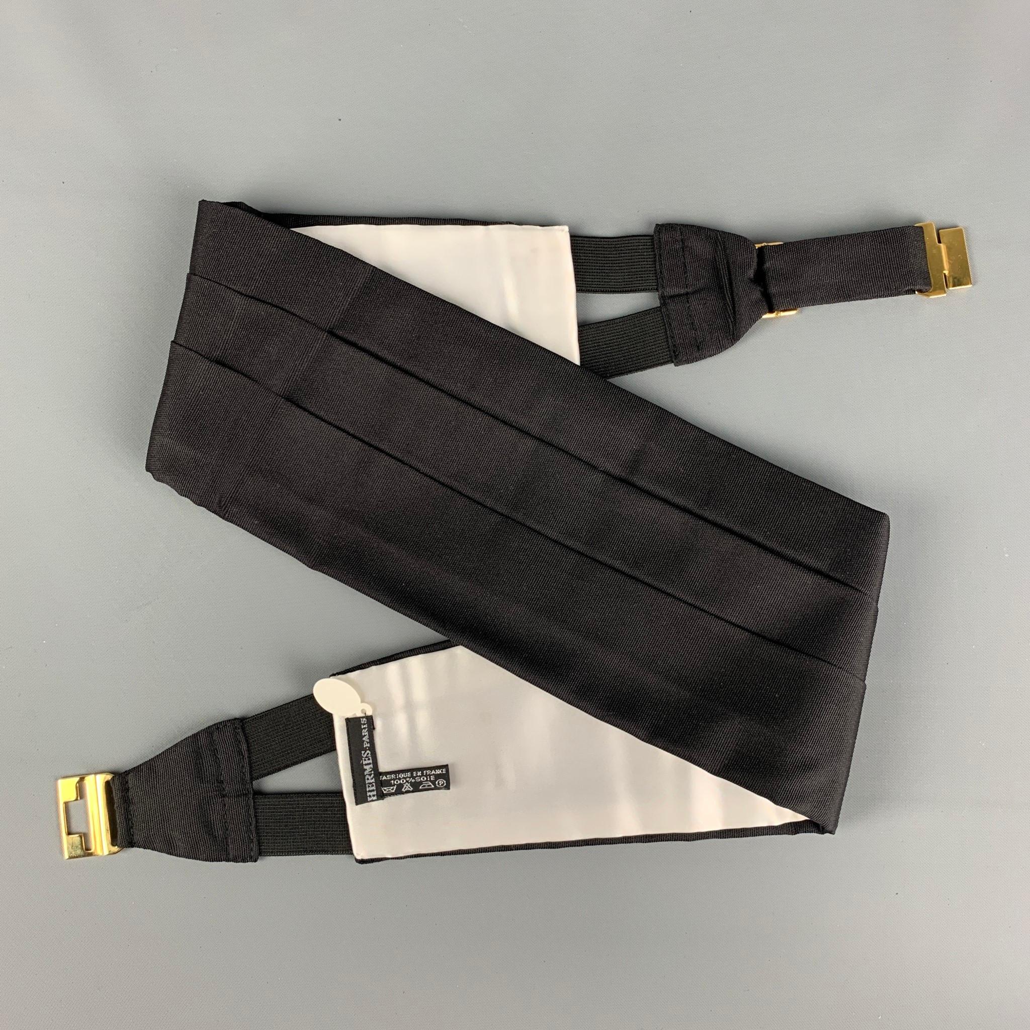 HERMES cummerbund set comes in a black pleated silk featuring a gold tone clasp and includes a matching bow tie. Made in France. 

New With Box. 

Measurements:

-Cummerbund. 
Height: 4.75 in.
Length: 36.5 in.

Bow Tie.
-Length: 35 in.