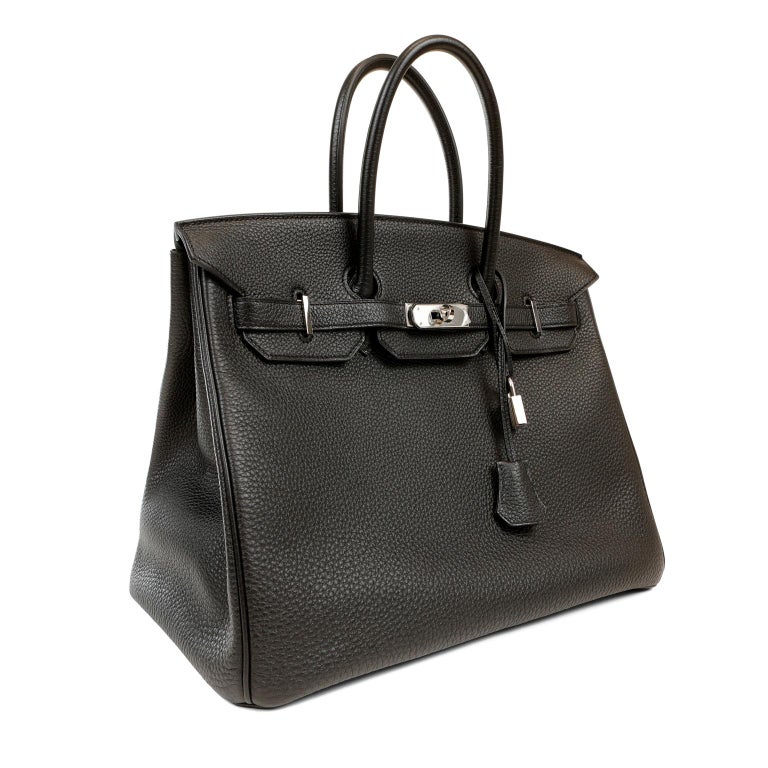 This authentic Hermès Black Togo 35 cm Birkin is in pristine condition with the protective plastic intact on much of the hardware.    Hand stitched by skilled craftsmen, wait lists of a year or more are common for the Hermès Birkin. They are
