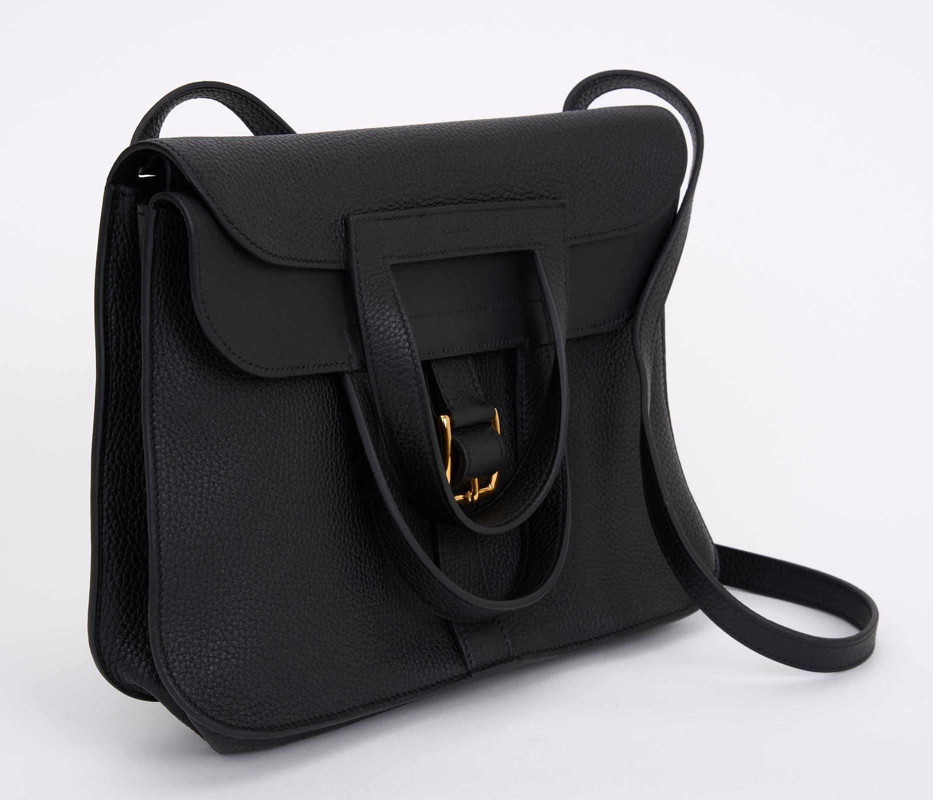 This Hermès Halzan 31  is crafted of black Taurillon Clemence leather and features an optional, adjustable leather shoulder strap, looping top handles, and a gold-plated buckle. The top opens to a smooth black leather interior with pockets. Comes