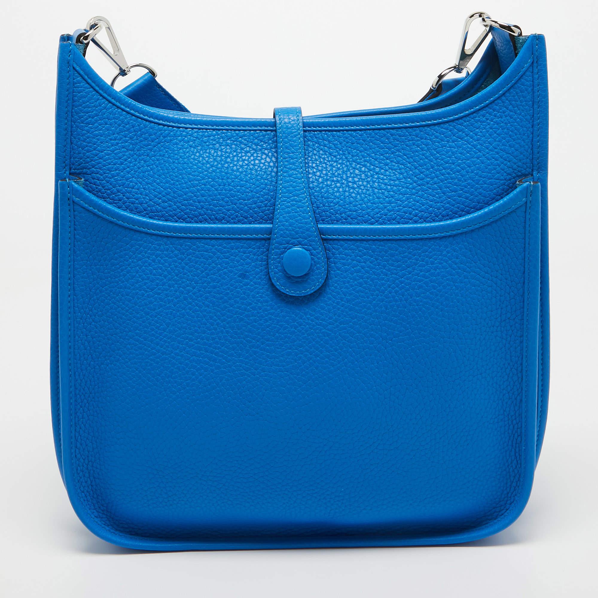 The Hermès Evelyne Bag is a luxurious accessory crafted with precision. Its vibrant blue hue, made from high-quality Taurillon Clemence leather, exudes sophistication. The Evelyne design features a perforated H logo, a spacious interior, and a