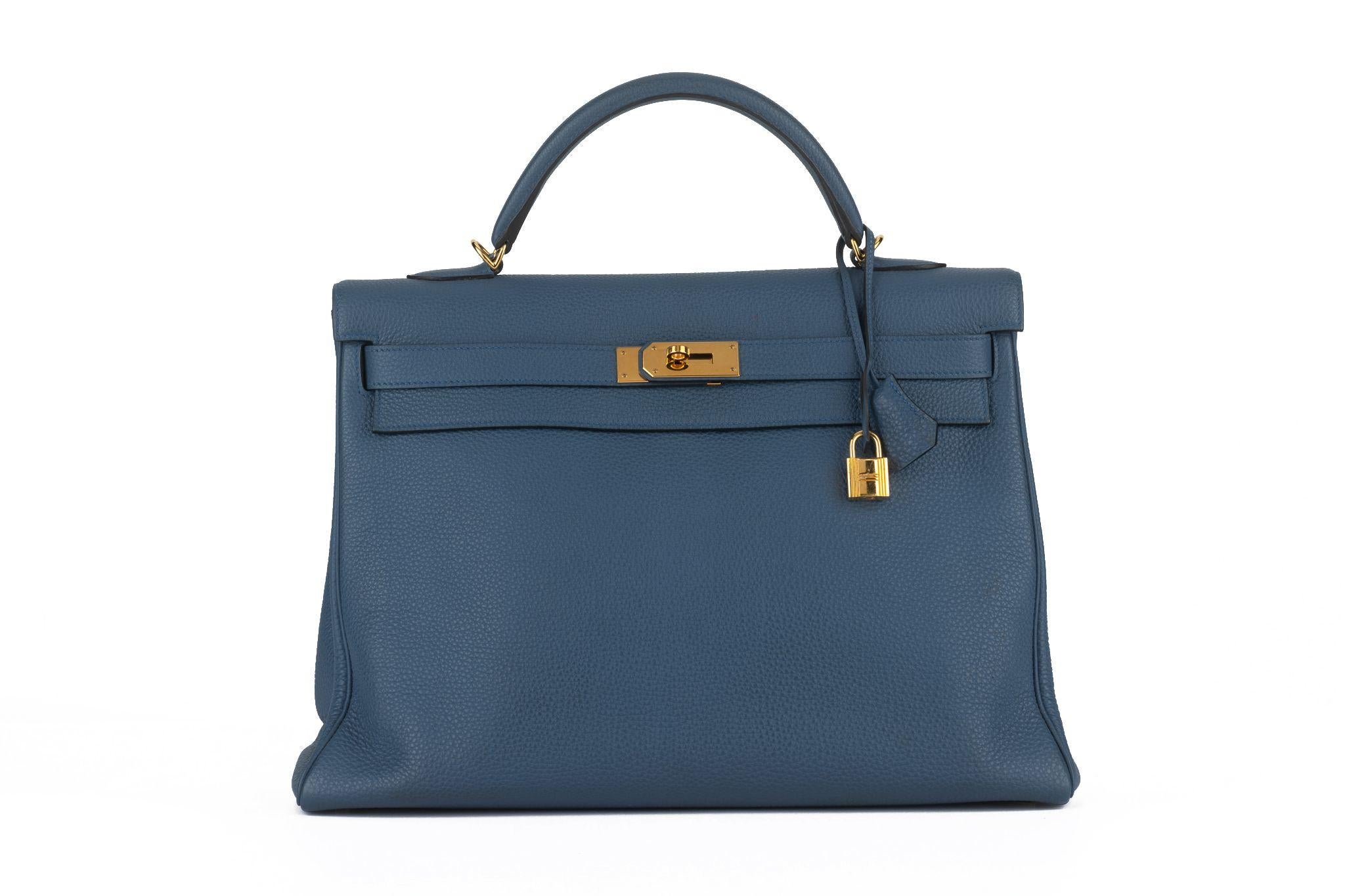 This Hermès Retourne Kelly 40 cm in Bleu brighton togo leather features a leather top handle with gold hardware, a crossover flap, and a strap closure with a gold signature Kelly turn lock, a padlock, a clochette and keys, and a shoulder strap. This