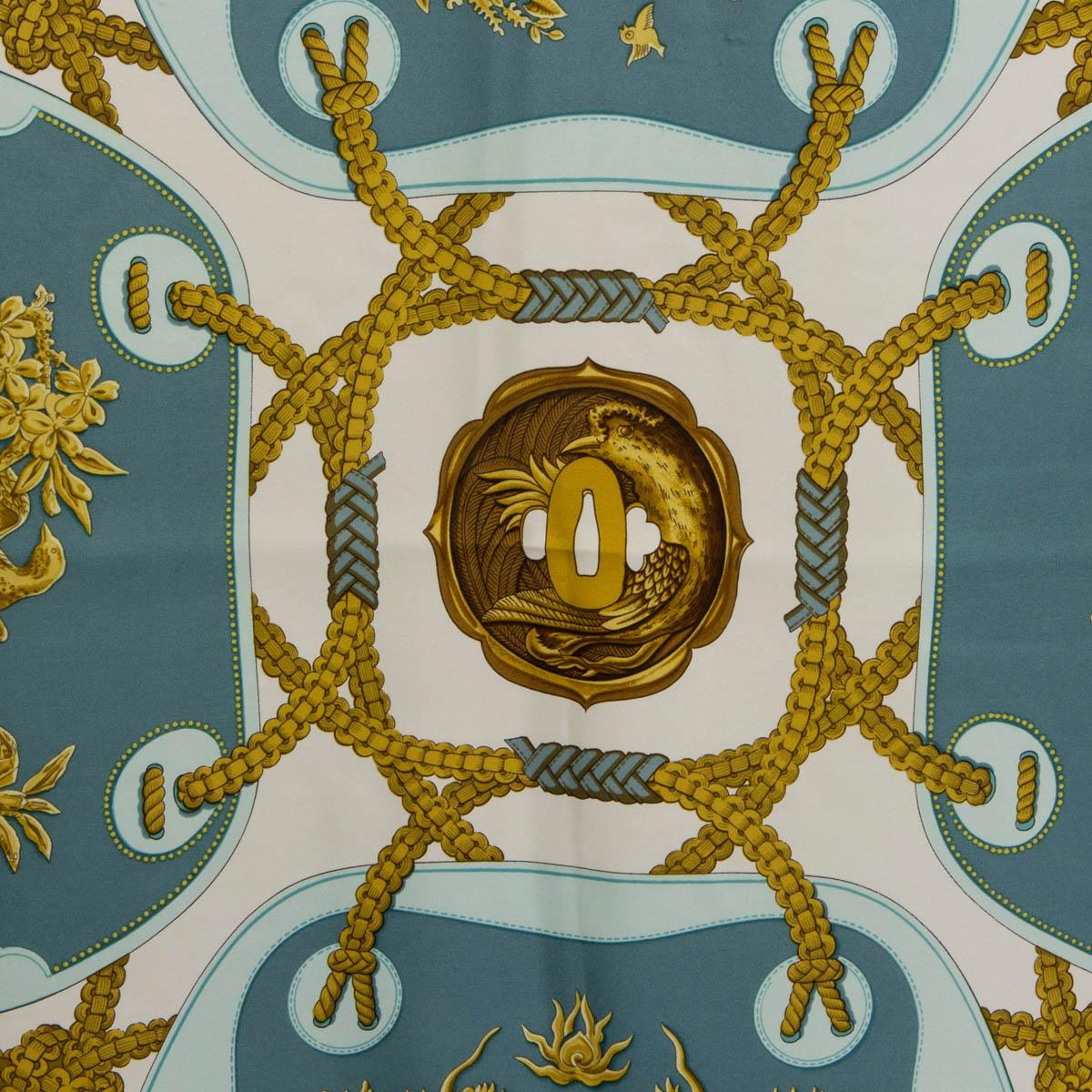 100% authentic Hermès Tsubas silk (100%) scarf designed by Christiane Vauzelles in pale blue, pale petrol and white with details in gold and brown. A tsubas is the handle or protective guard of a Japanese sword, typically embellished with carvings