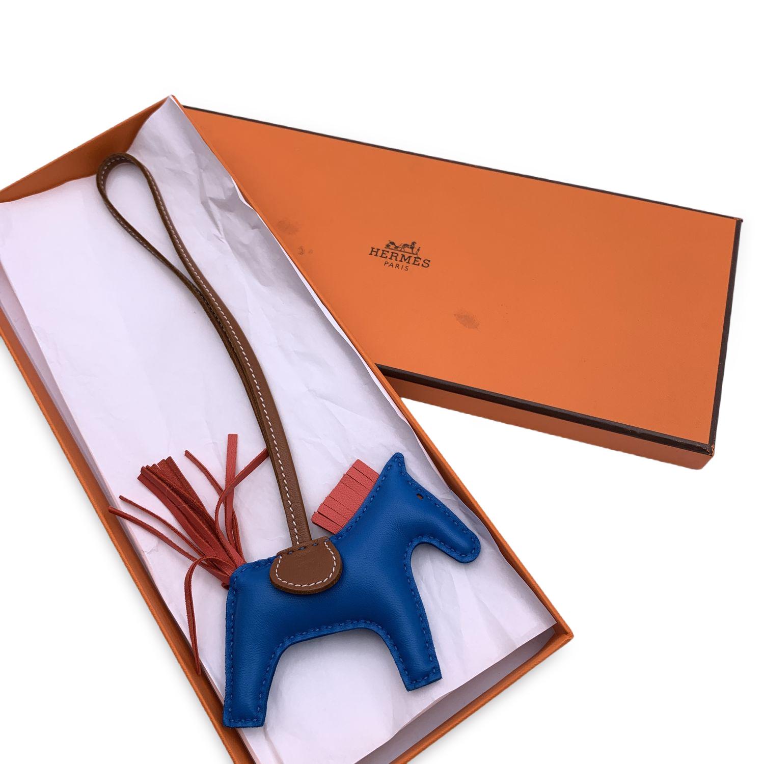 Hermes Rodeo PM Bag Charm Accessory in the shape of a horse. Body in blue leather, hair and tail in salmon red/pink color and saddle and loop in light brown color. Width: 3.5 inches - 9 cm. Height: 3 inches - 7.5 cm. 'Hermes Paris - Made in France'