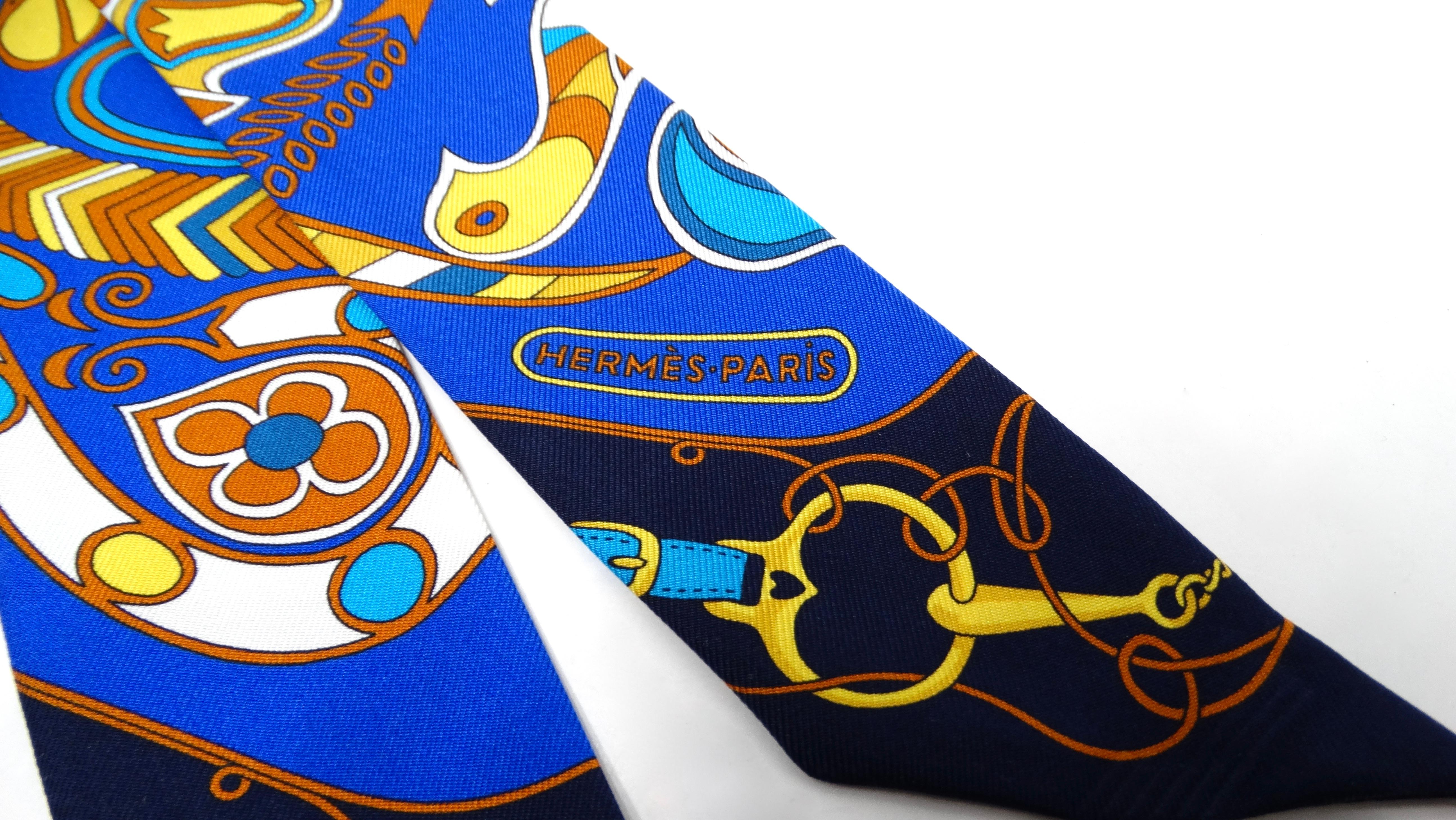 The Hermes Blue & Yellow Folklore Print Silk Twilly is a vibrant accessory that adds a touch of artistic flair to any ensemble. Featuring an abstract floral folklore print in a captivating palette of blues, yellows, and warm orangey browns, this