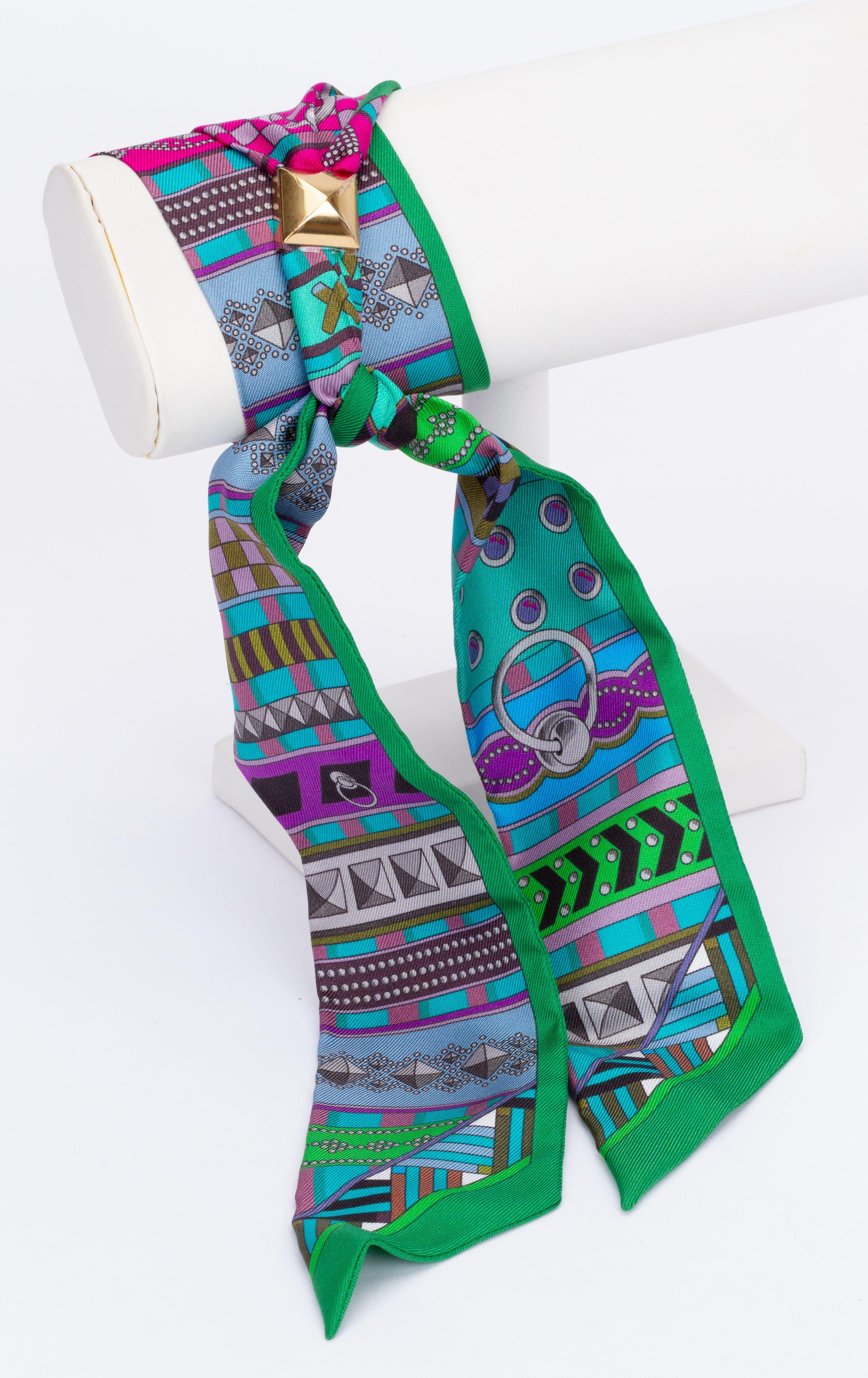 New Hermès Architecture Twilly. The scarf is made out of silk and is multicolor. The print shows different forms and architectural lines. The pieces comes with a scarf ring, the original box and ribbon.
