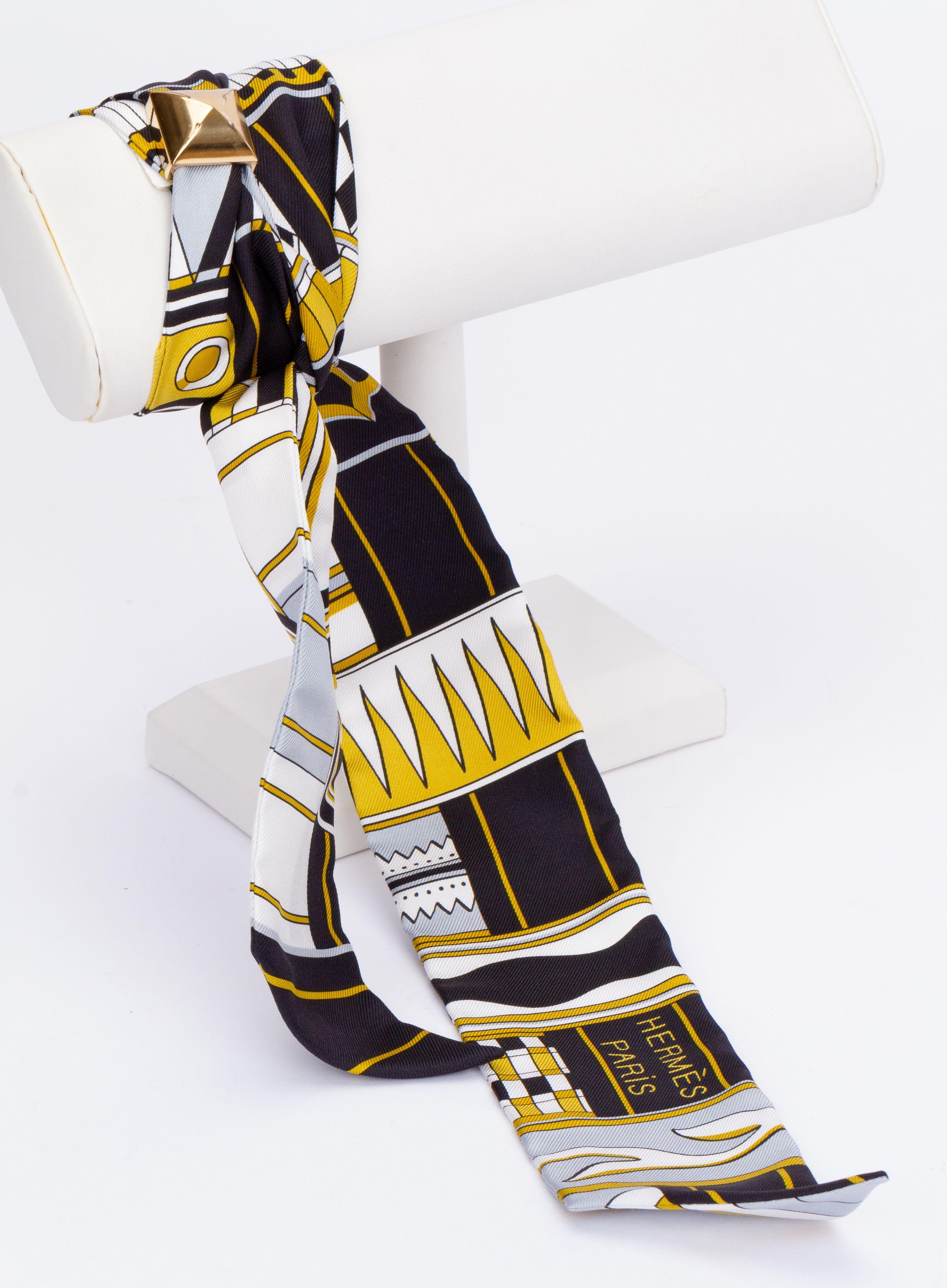 New Hermès Geometric Twilly. The scarf is made out of silk and the main color is yellow. The print shows different geometrical figures. It is brand new and comes with a scarf ring. It is packend in the original box and wrapped with the traditional