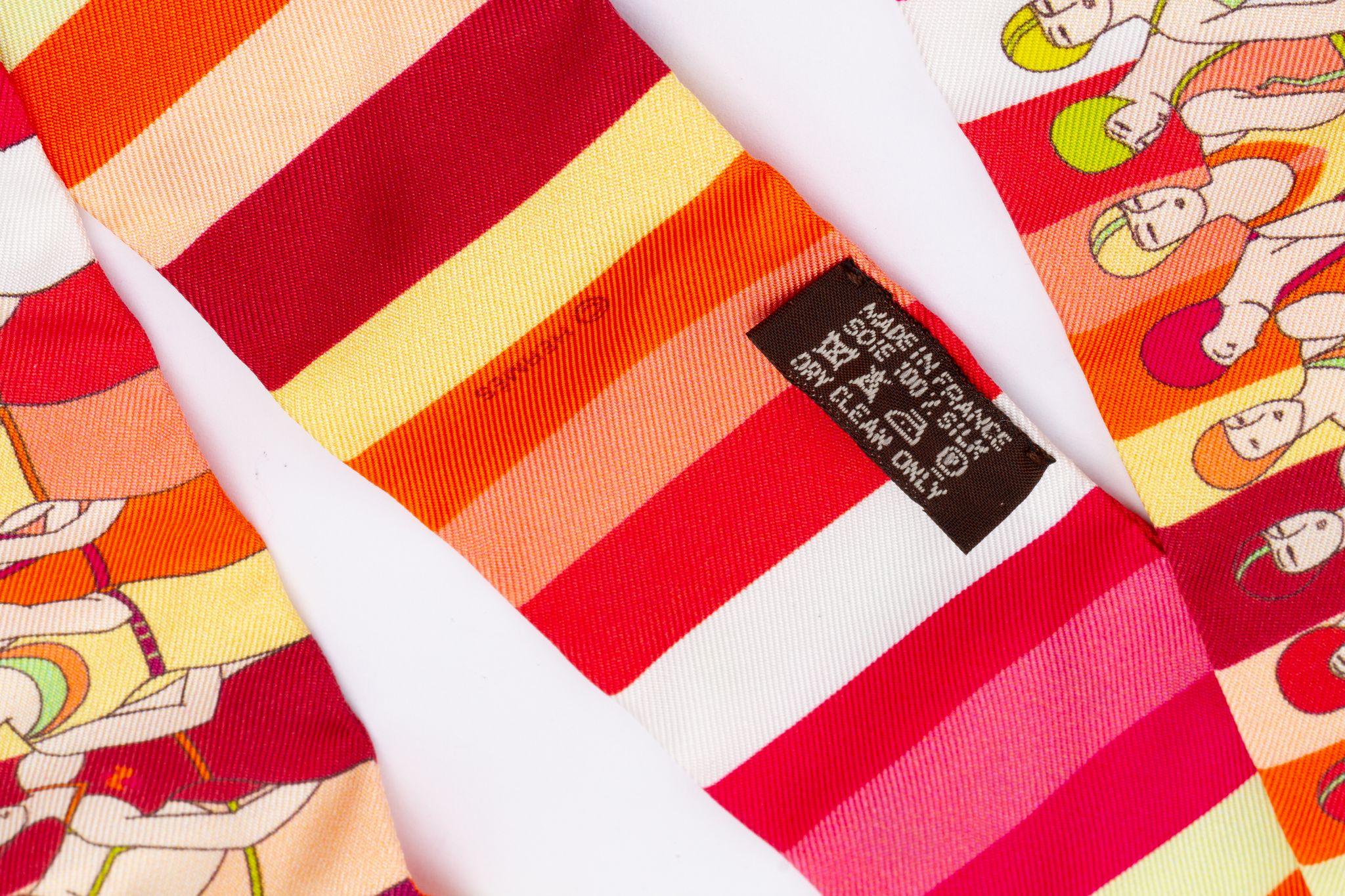 Nuovo Hermès Swimmers Edition Twilly. La sciarpa è realizzata in seta e il colore principale è un rosso e un arancione vivaci. La stampa mostra una fila di nuotatori. Viene fornito con un anello per sciarpa, la scatola originale e il nastro.