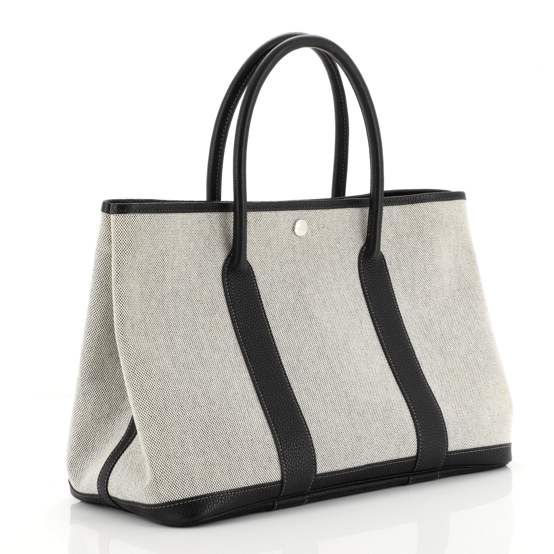 This Hermes Bolduc Twilly Garden Party Tote Toile and Leather 36, crafted from Noir black Buffalo Skipper leather and neutral Toile H, features dual rolled handles, side snap buttons and palladium hardware. Its snap button closure opens to a Rouge H