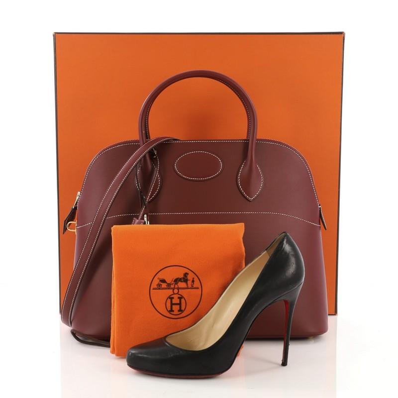 This Hermes Bolide Handbag Chamonix 35, crafted from Rouge H Chamonix leather, features dual rolled leather handles, protective base studs, and gold hardware. Its zip closure opens to a Rouge H Agneau leather interior with slip pocket. Date stamp