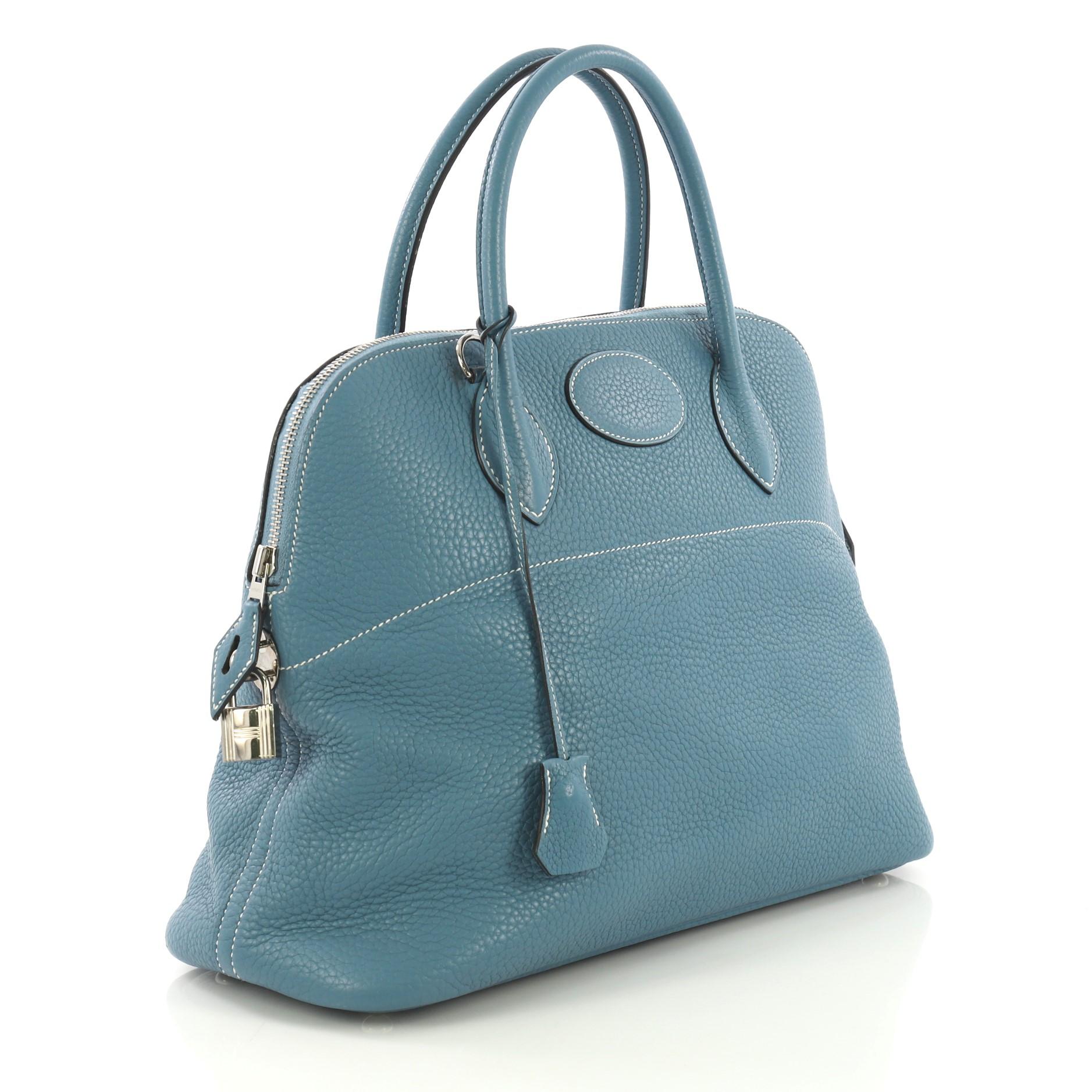 This Hermes Bolide Handbag Clemence 31, crafted from Bleu Jean blue Clemence leather, features dual rolled leather handles, protective base studs, side lock, and palladium hardware. Its zip closure opens to a Bleu Jean blue Agneau leather interior.