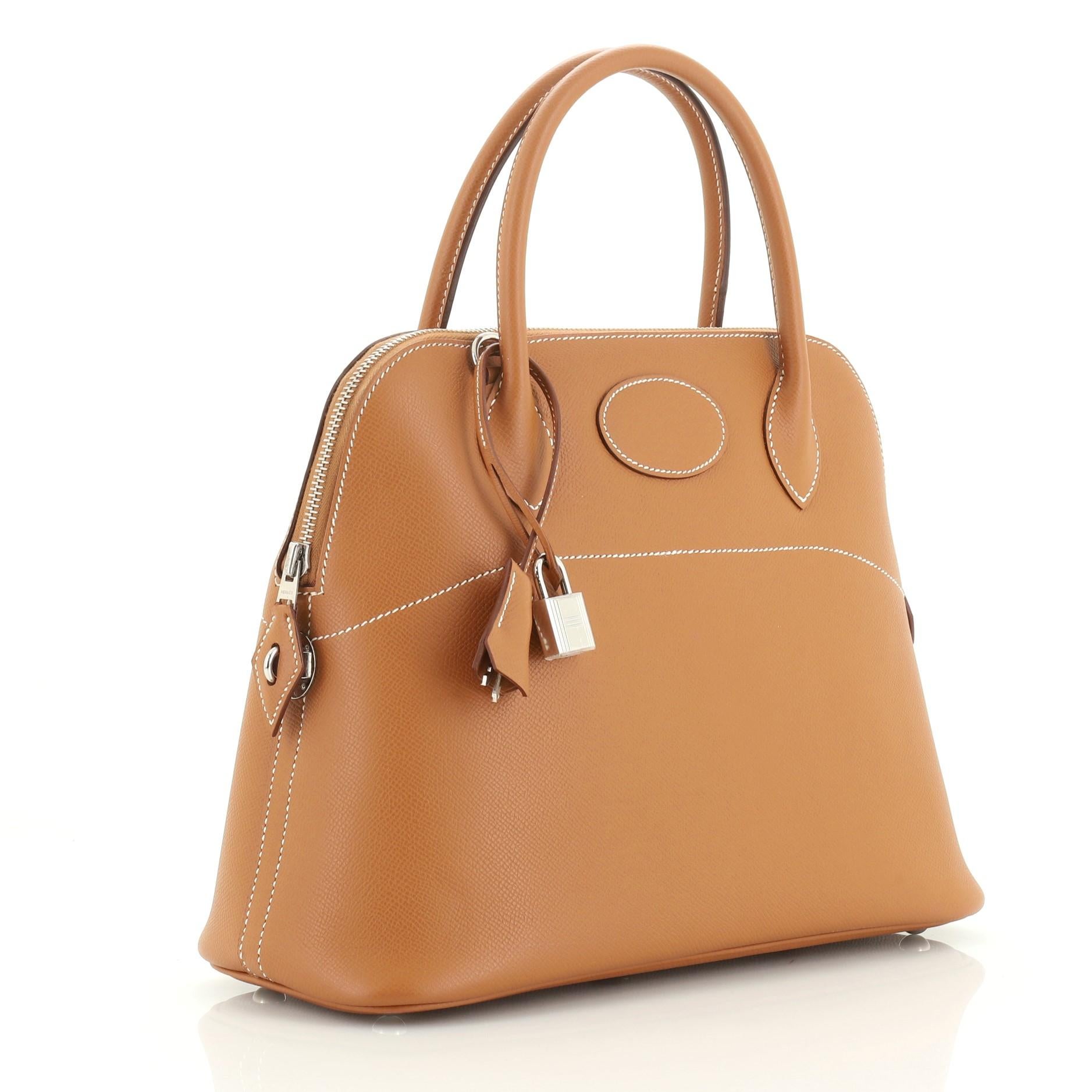 This Hermes Bolide Handbag Epsom 31, crafted from Gold brown Epsom leather, features dual-rolled leather handles, protective base studs, side lock hardware and palladium hardware. Its zip closure opens to a Gold brown Agneau interior. Date stamp