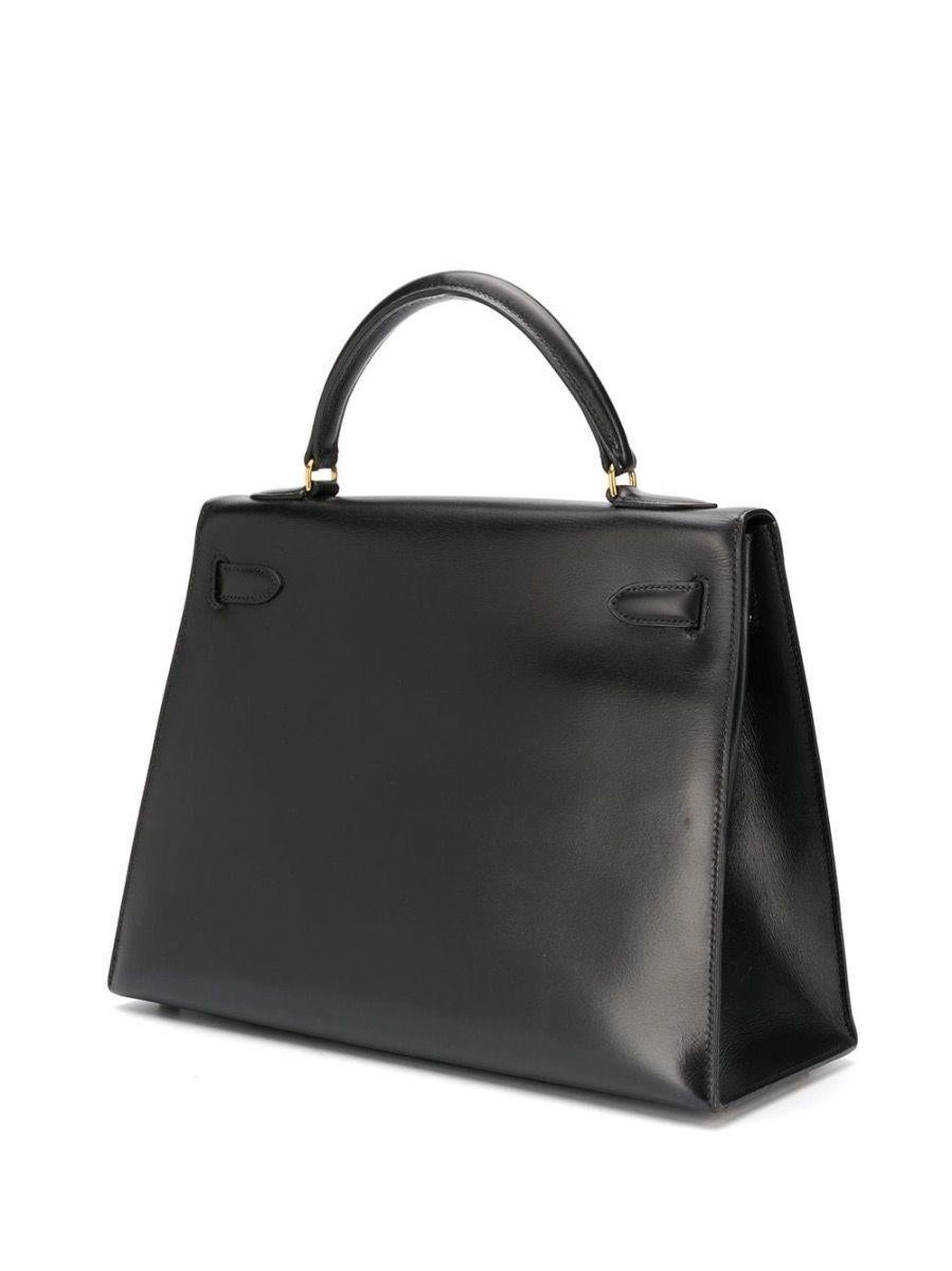 Meticulously crafted in France from smooth black box calf leather, a favoured Hermès hide for its smooth texture and glossy finish, this unique piece features a trapeze-shaped body, a medium top-handle and gold-tone metal accents. 32cm in width, the