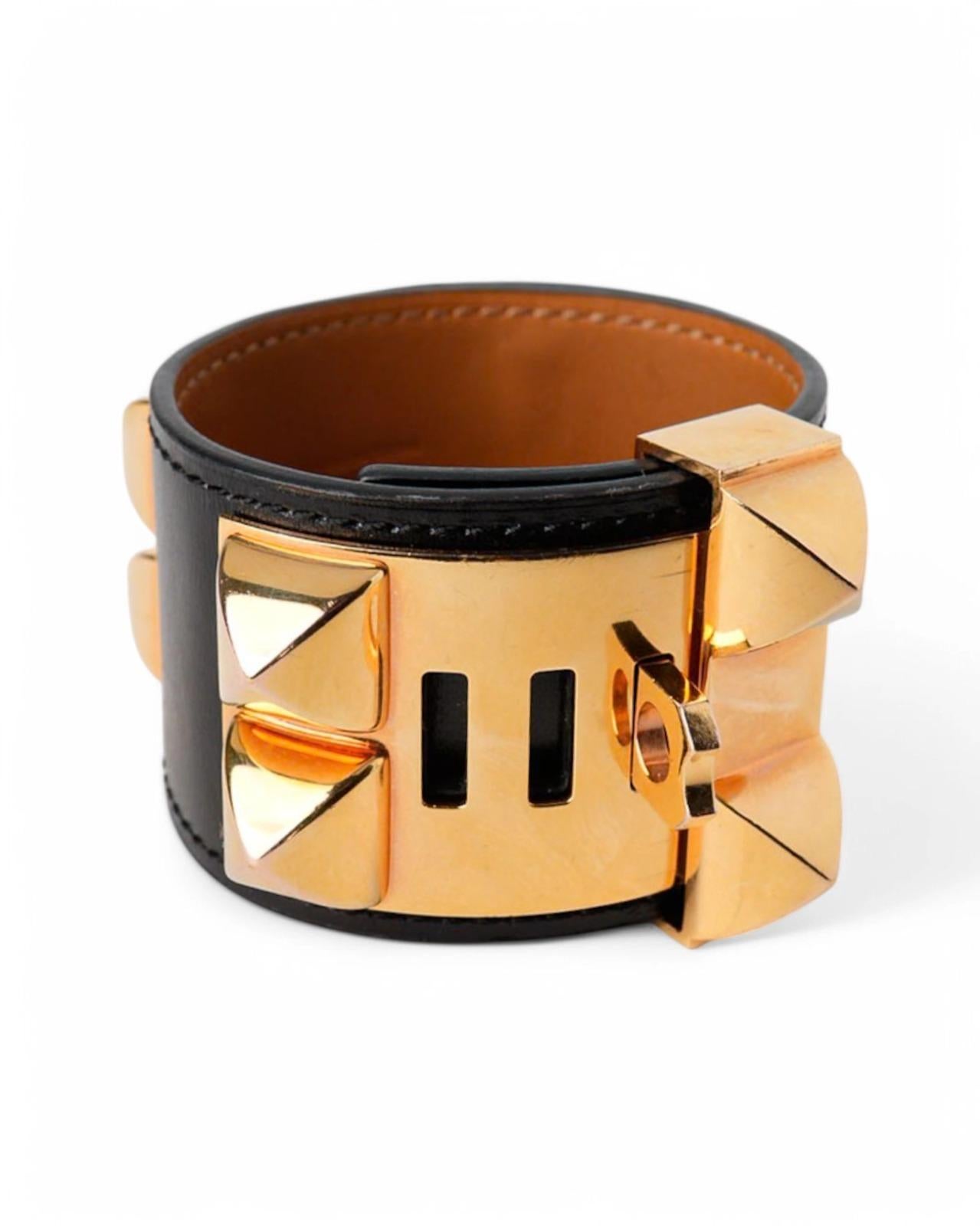 Pulsera de la firma Hermès, modelo Collier De Chien, realizada en fina piel de caja negra y adornada con tachuelas doradas. Esta pulsera ajustable ofrece un diseño atrevido y sofisticado, perfecto para añadir un toque de lujo a cualquier atuendo. El