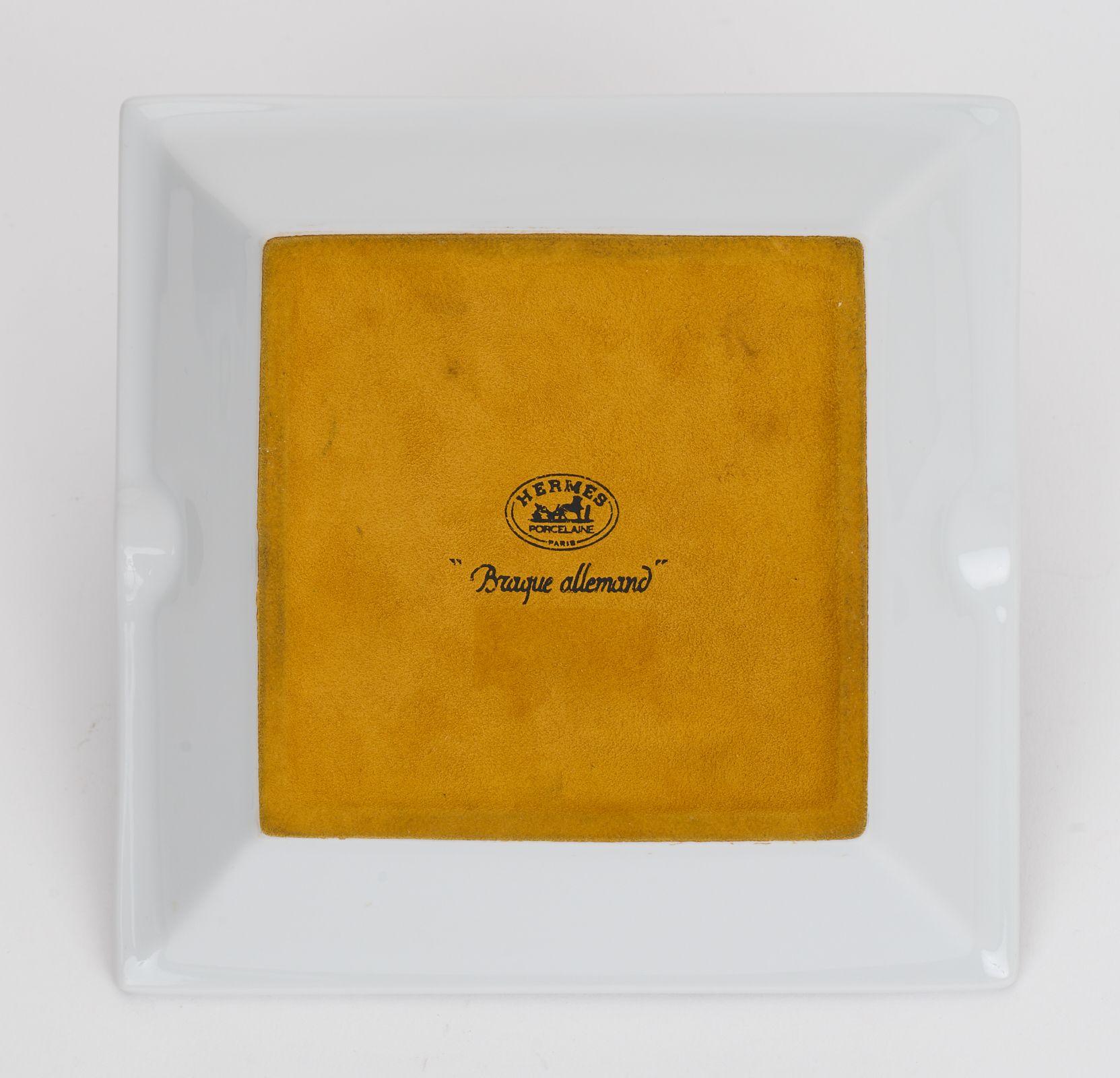 Questo posacenere in porcellana Hermès Braque Allemand Dog raffigura un Pointer tedesco a pelo corto in posizione di caccia, bianco con bordo giallo e bordi marroni. Il vassoio ha un fondo protettivo in pelle scamosciata.