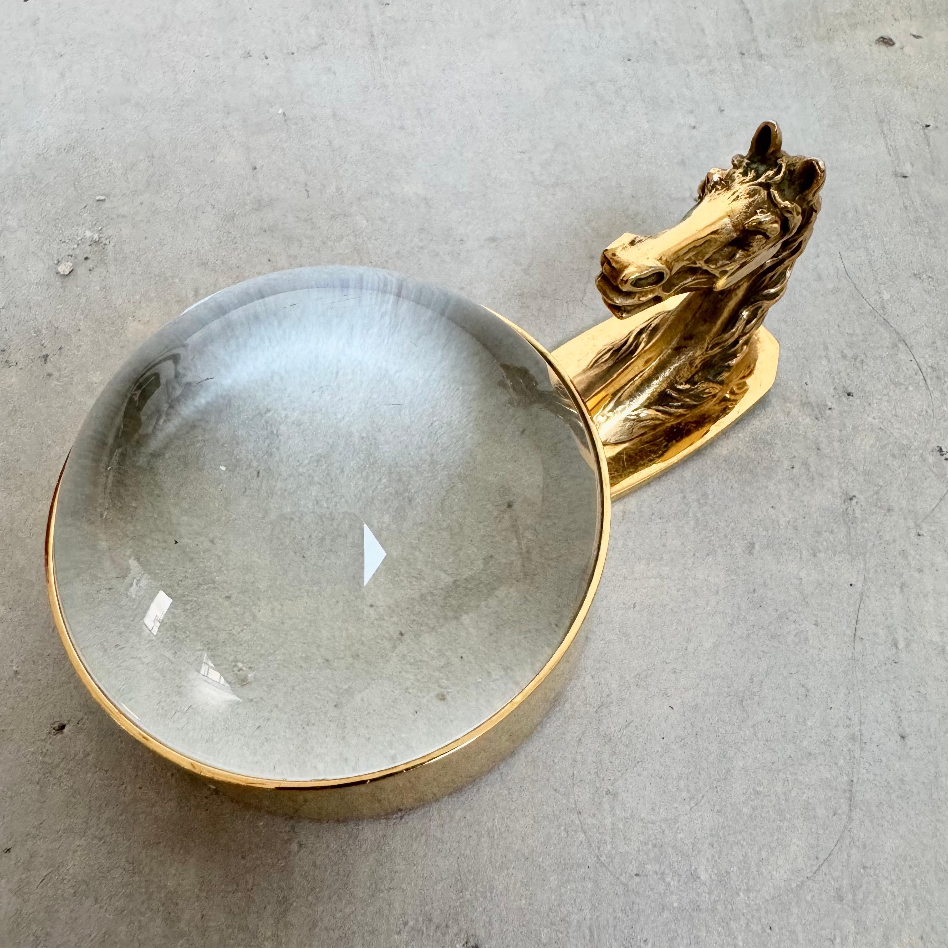 Elegant equestrian Hermès magnifying glass with Hermès Paris stamped on the base. Features an engraved horse head handle and a substantial magnifying glass. The frame is solid brass with a very light patina.

This piece is a stunning and practical