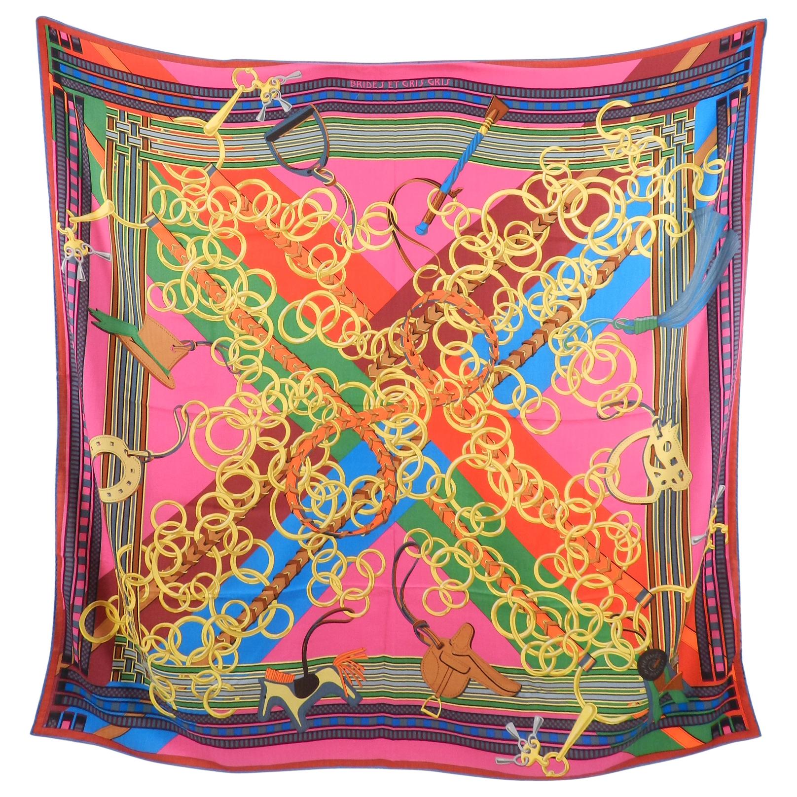 Hermes “Brides et Gris Gris” Cashmere Blend Shawl 140cm.  Vibrant design in fuchsia, red, blue, green, yellow, and orange.  Chain horse bridle design with various Hermes bag charms.  Excellent pre-owned condition with a small pull at centre bottom