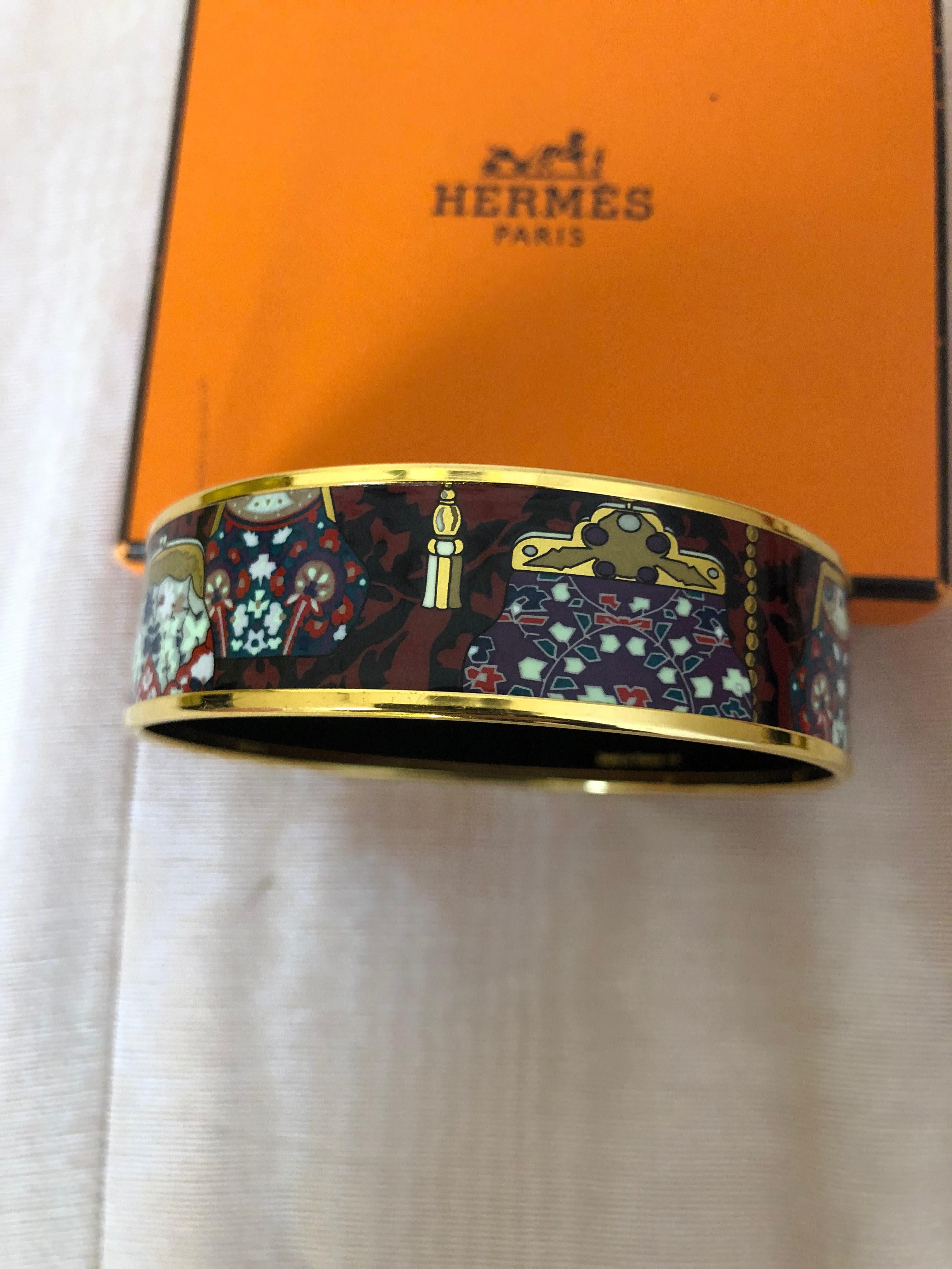 This Hermes Cachmire de Tamara bangle is made of enamel and gold plated rims and is well marked. The beautiful graphics are of vintage evening bags and florals. The bangle is size GM 70 8 M-L, is in excellent condition, and comes with a dustbag and