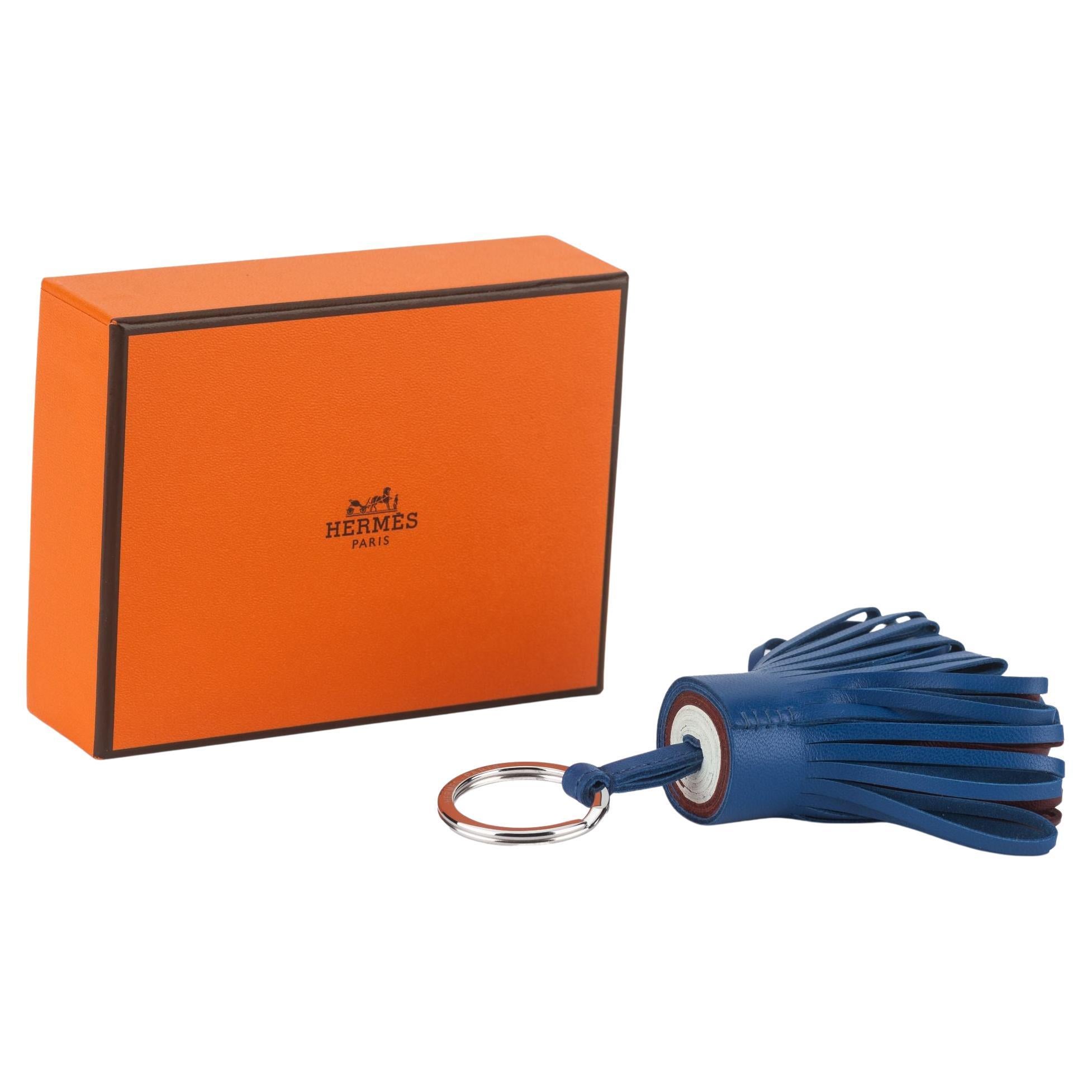 Este llavero con borla Carmen de piel de cordero Hermès tiene una pequeña borla de suave piel de cordero en color bleu y un llavero plateado. Viene con caja original. A estrenar.