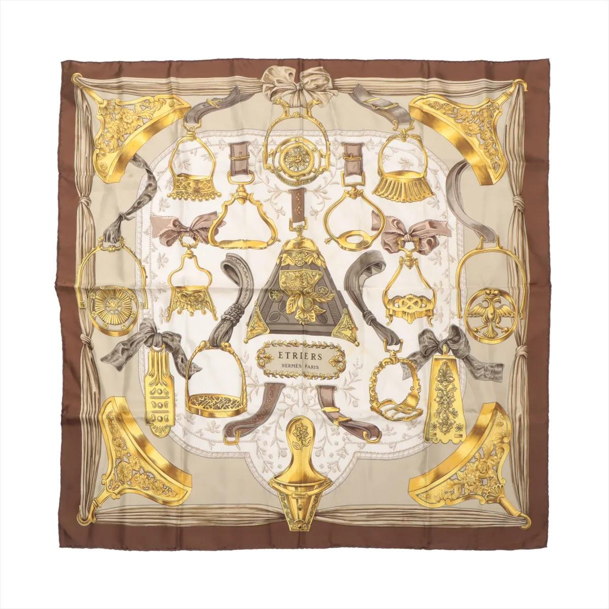El Pañuelo de Estribo de Seda Hermès Carré 90 d'Etriers en Marrón es una impresionante muestra de la herencia ecuestre y la maestría artística de la Maison. Confeccionado en lujosa seda, presenta el clásico diseño d'Etriers, una intrincada