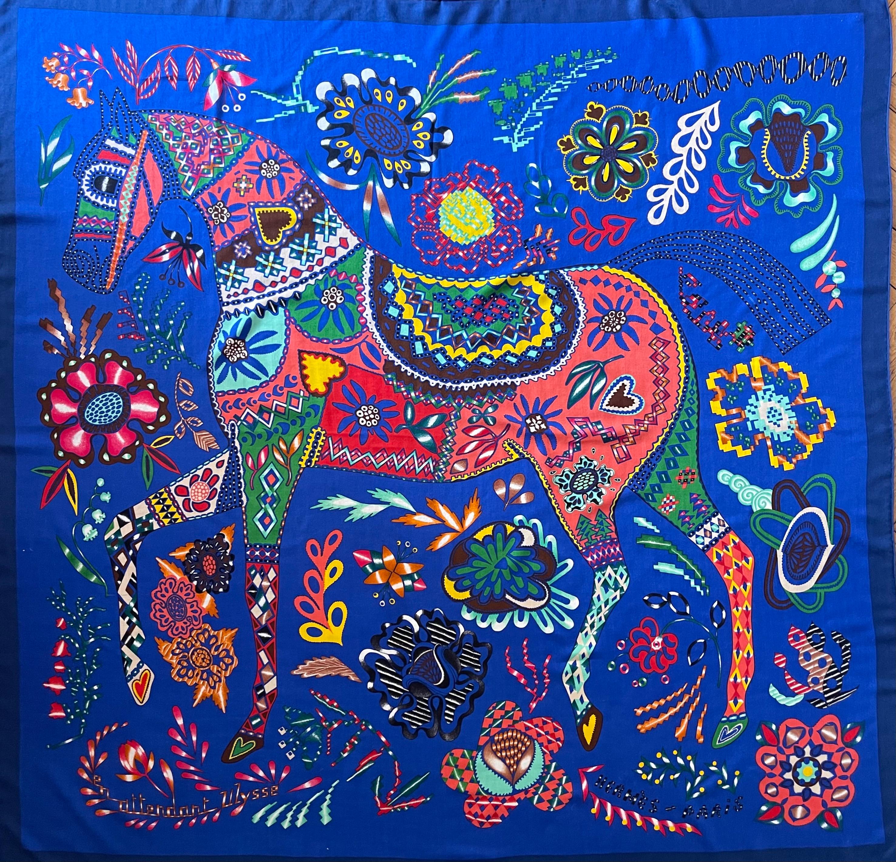 Hermès Cashmere scarf “En Attendant Ulysse”.  This chic scarf depicts an elaborate graphic design that incorporates a bold design in various tones of blue. Florence Manlik designed this scarf inspired by Eastern European folklore and the motifs of