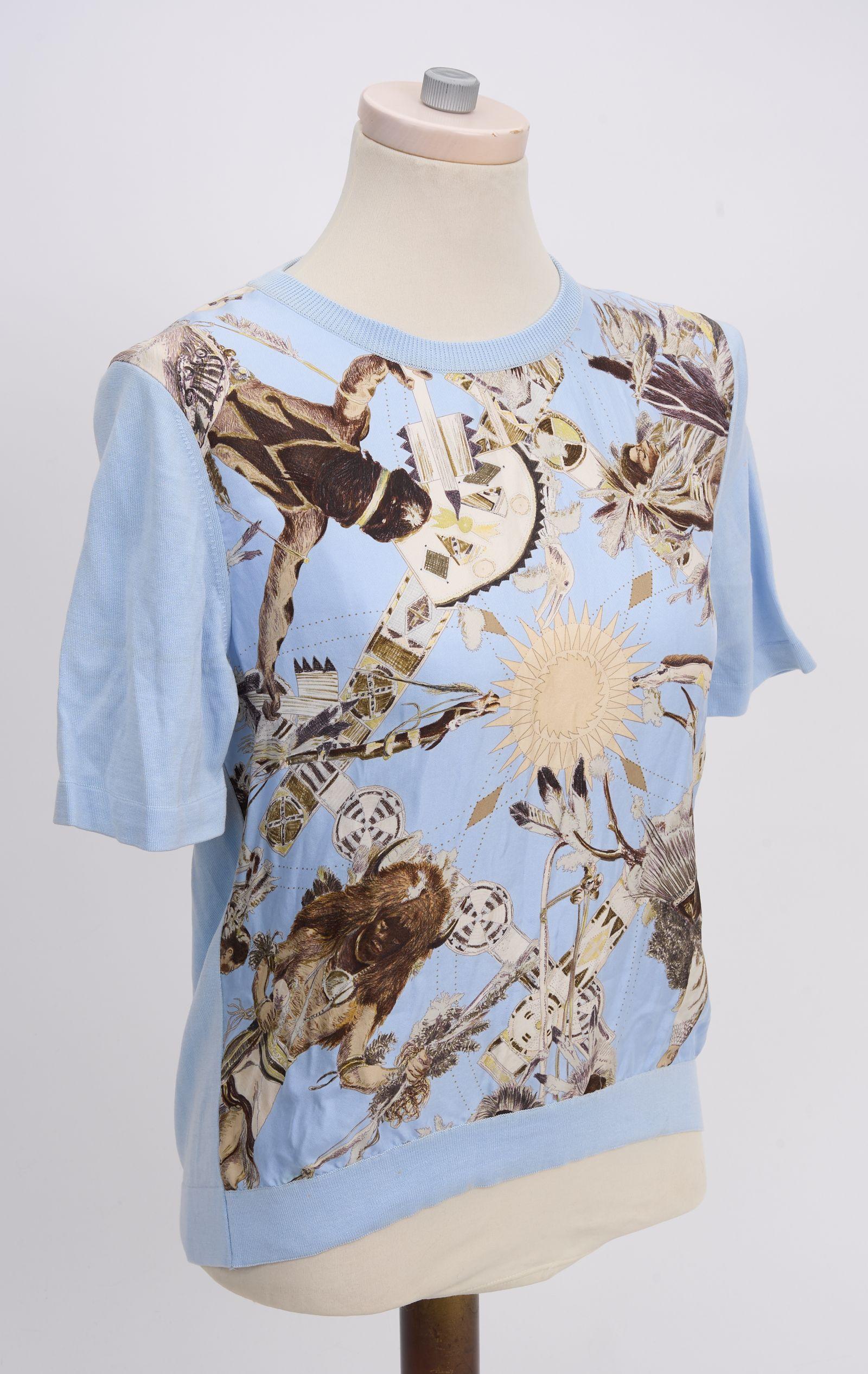 This Hermès Celeste Mythologie Silk Shirt features a tribal print down the front, the hem, arms and neckline are trimmed with croton. Collectible design by famous Texas artist Kermit Oliver. A single button closure on back. Size M

Shoulder -