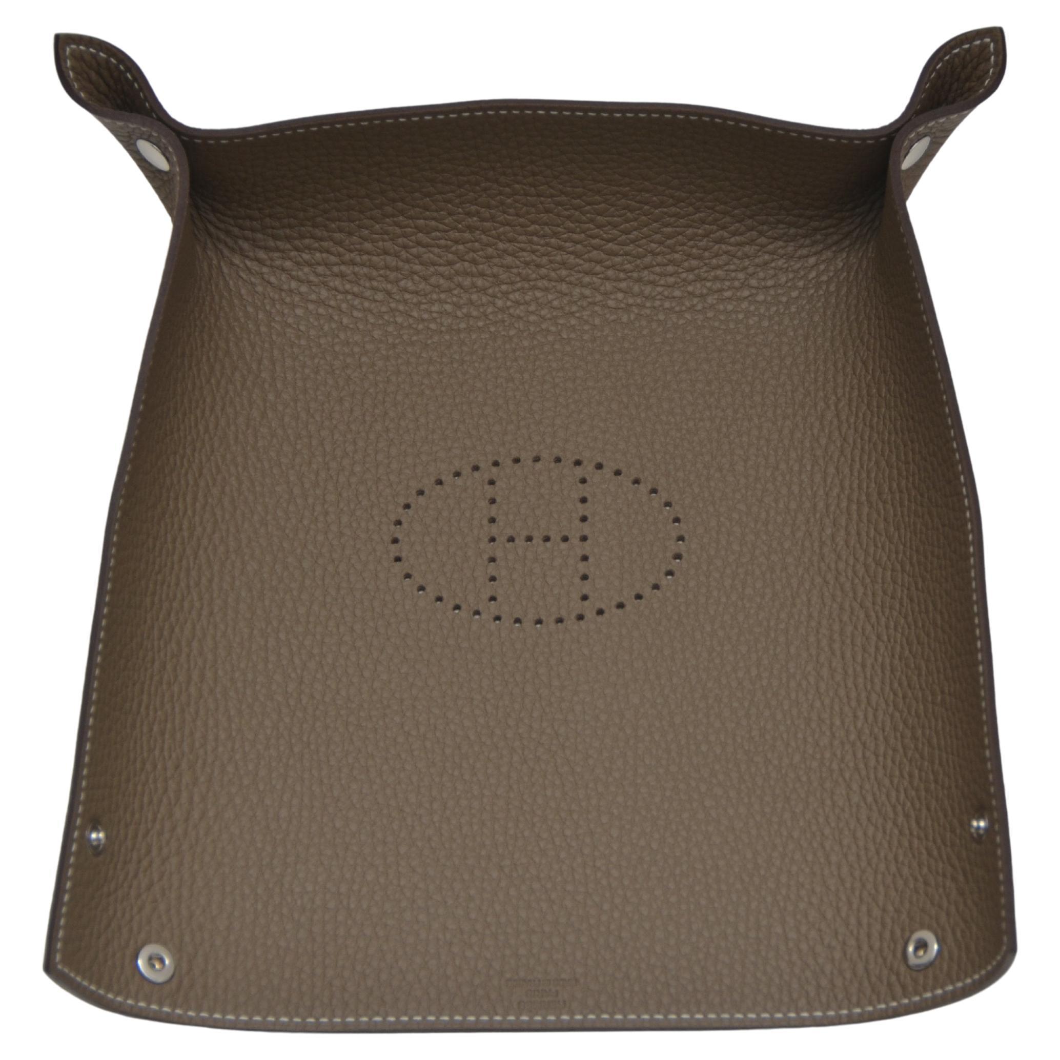 Hermes change tray with perforated Evelyn H.
Beautifully crafted featuring Etoupe in Clemence leather.
Nickeled clou de selle snaps.
A beautiful desk or bedroom accessory.
Stamped Hermes Made in France.
New or Store Fresh Condition.
Mightychic is