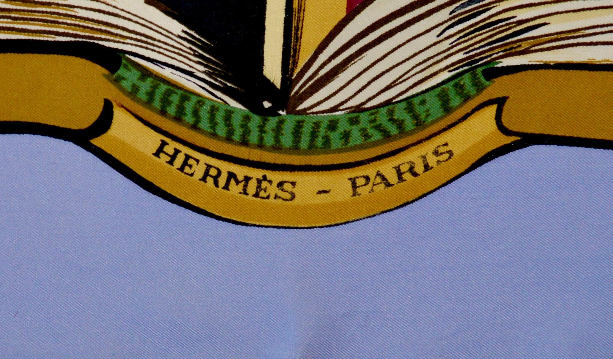 A wonderful Hèrmes silk scarf first designed in 1962 by Lise Coutin. Depicting an image of an open book filled with coats of arms, monograms and heraldic symbols finished in lilac, black, gold, green and madder rose colourway. 
Marked Hermes Paris