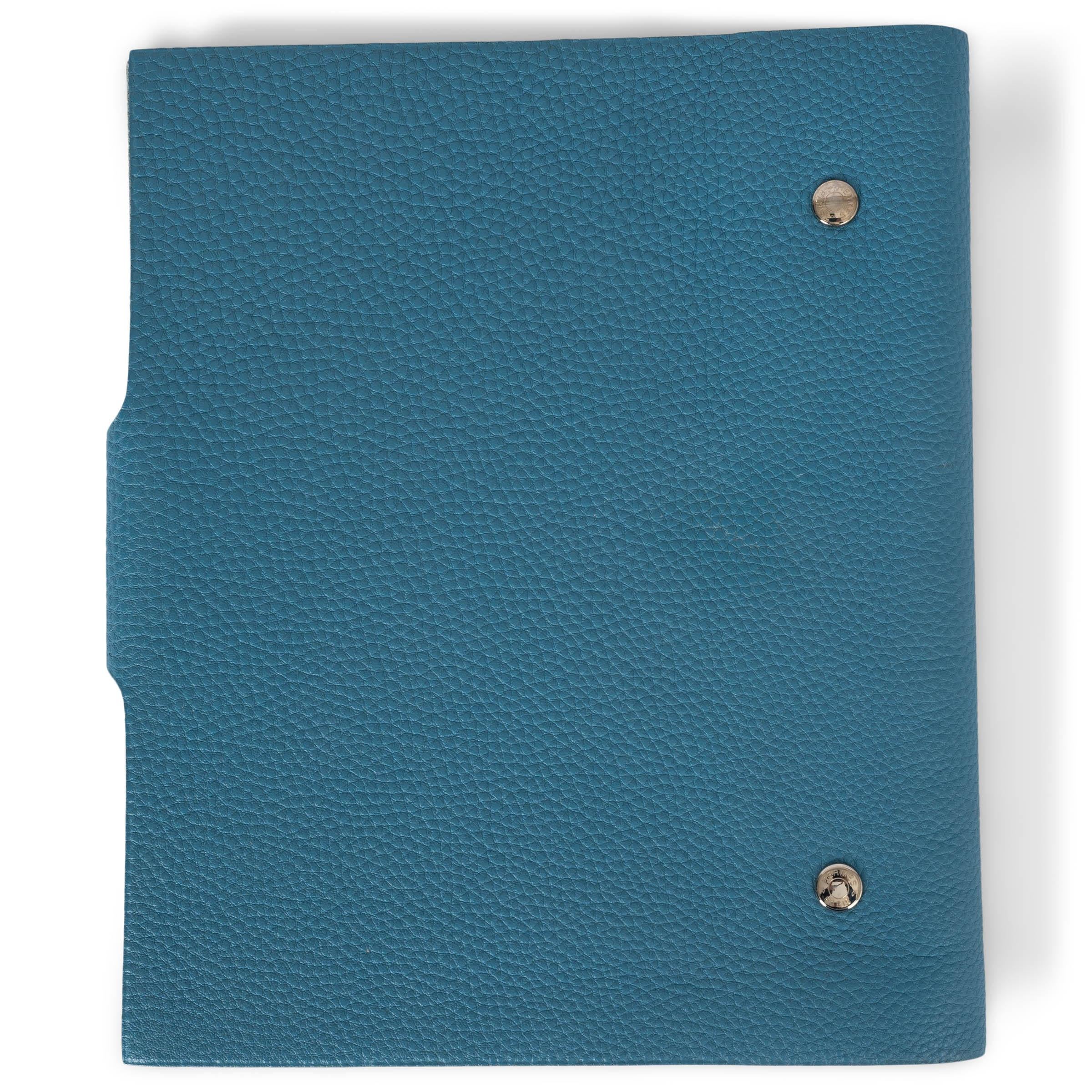 This 100% authentic Hermès Ulysse MM agenda cover is crafted from Bleu Ciel (dusty blue) Veau Togo leather, offering a refined and timeless design. It features a palladium Clou de Selle snap-button closure, adding a touch of elegance to this