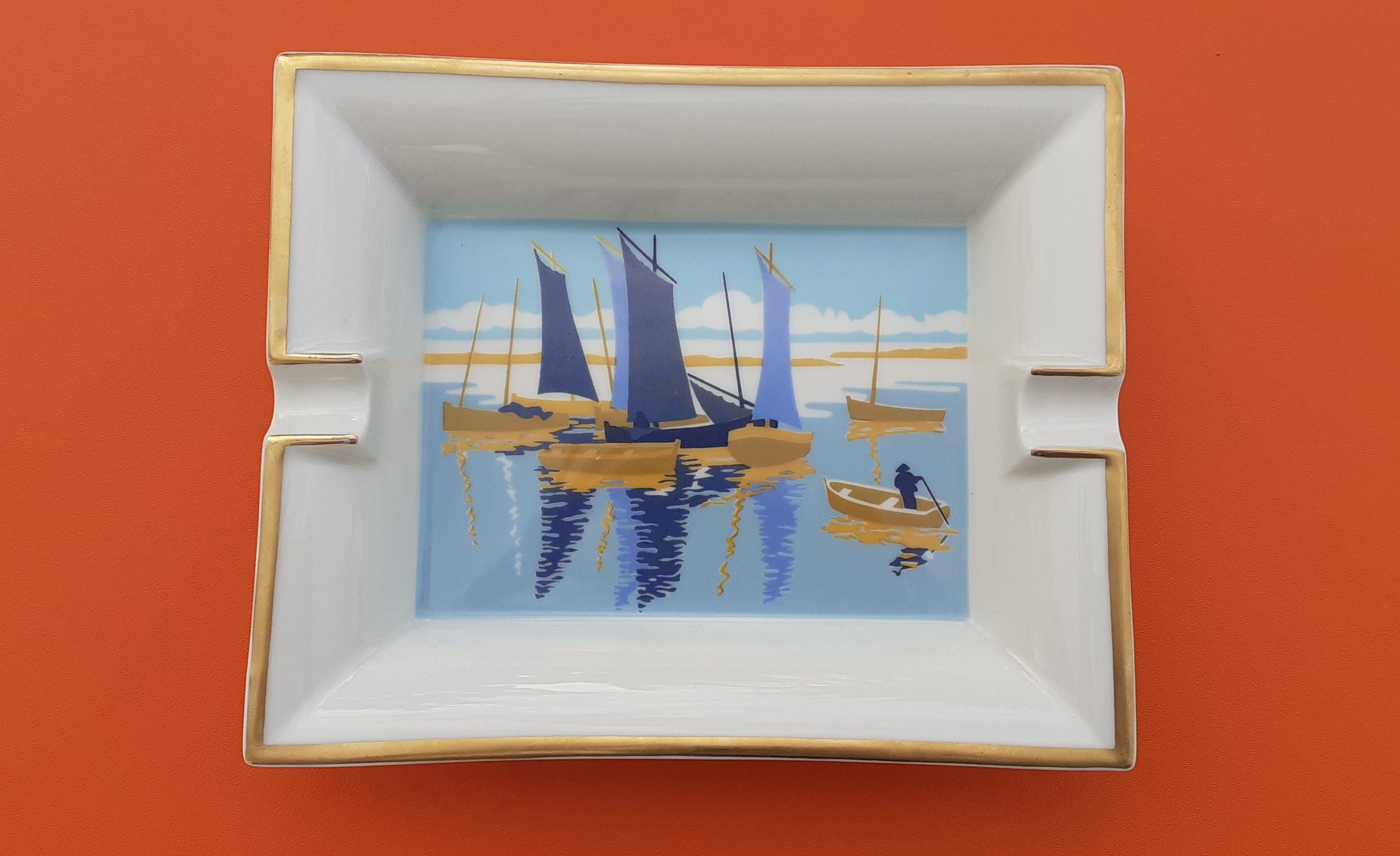 Beautiful and Rare Authentic Hermès Ashtray

Print: Small Boats / Sailing Ships

Made in France

Made of porcelain, edges gilded with fine gold

Colorways: Golden / White / Blue / Yellow

Dark suede leather at bottom

