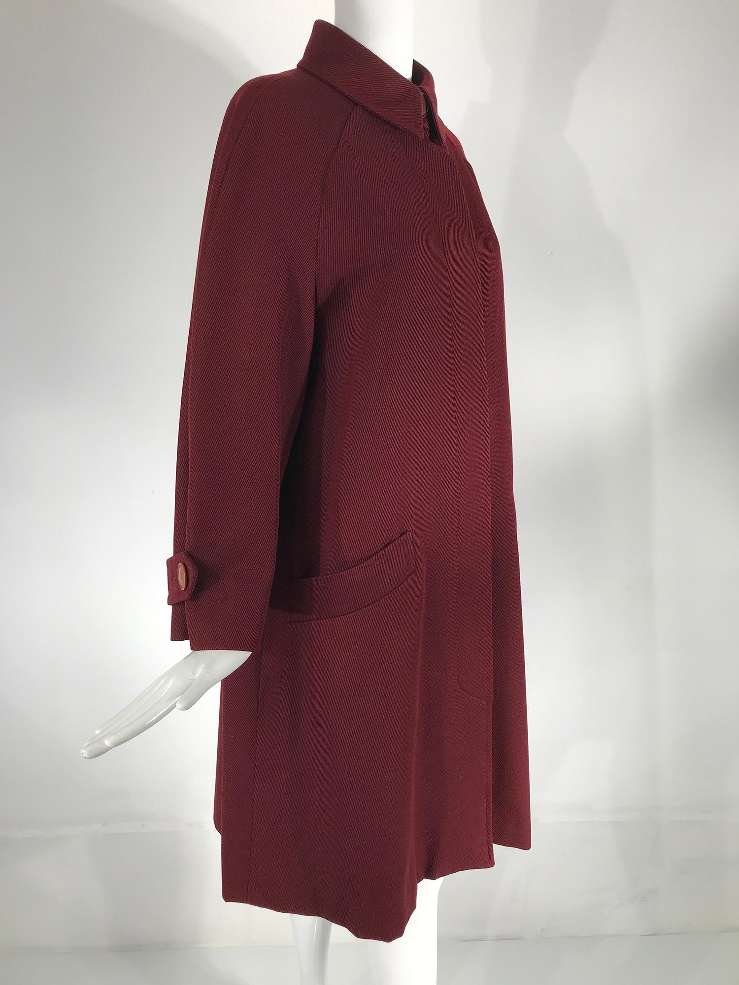 Hermes classic burgundy wool twill over coat a timeless addition to any wardrobe. Long raglan sleeve coat with Hermes logo button tab cuffs. Round collar with a logo button at the neck, hidden button placket front closure, with Hermes logo buttons.