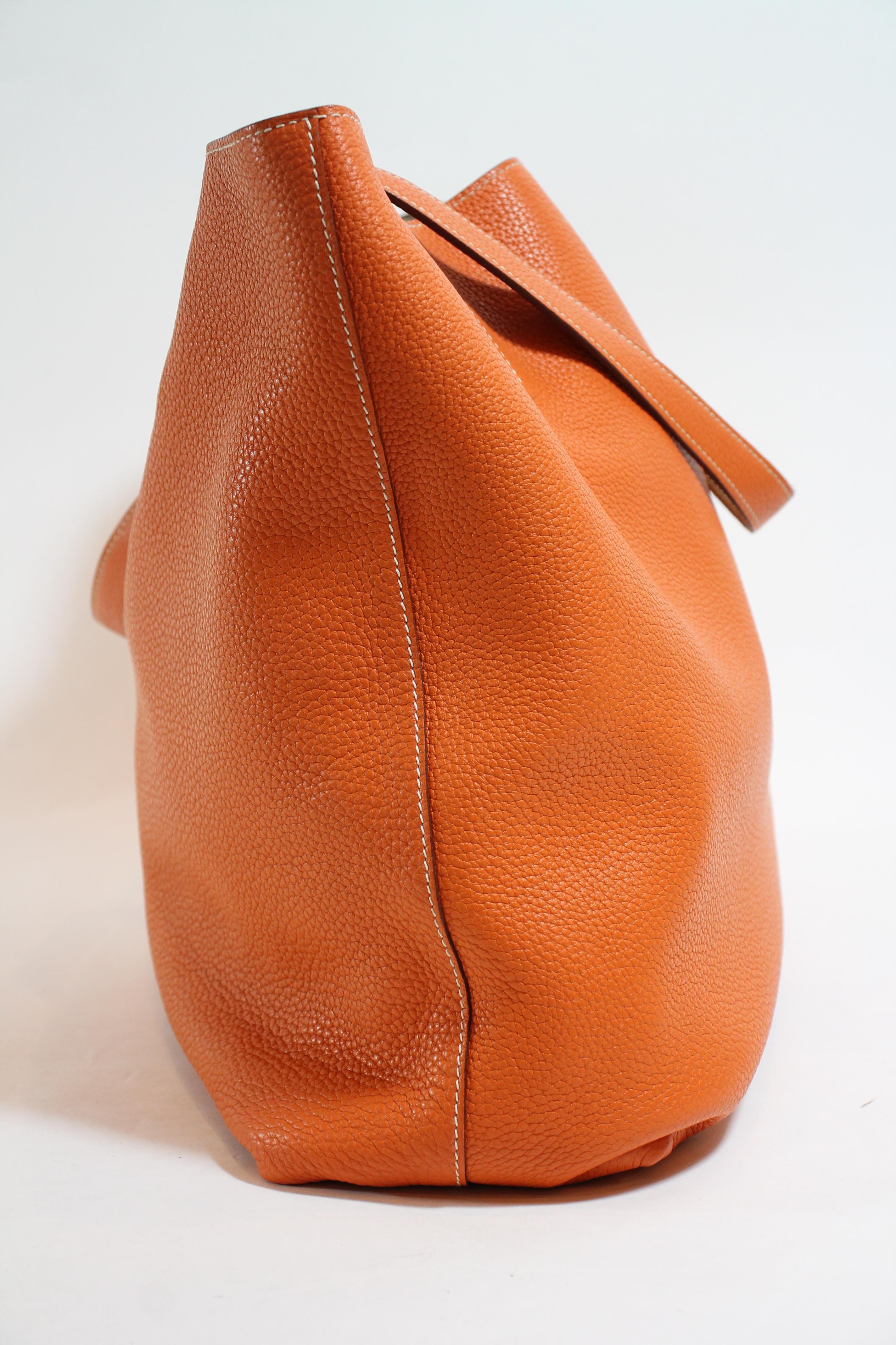 Orange d'H Clemence leather. Contrast stitching throughout. Open top. Dual flat shoulder straps. Foil-stamped logo accent at front face, Gold Clemence leather interior. Blind stamped.