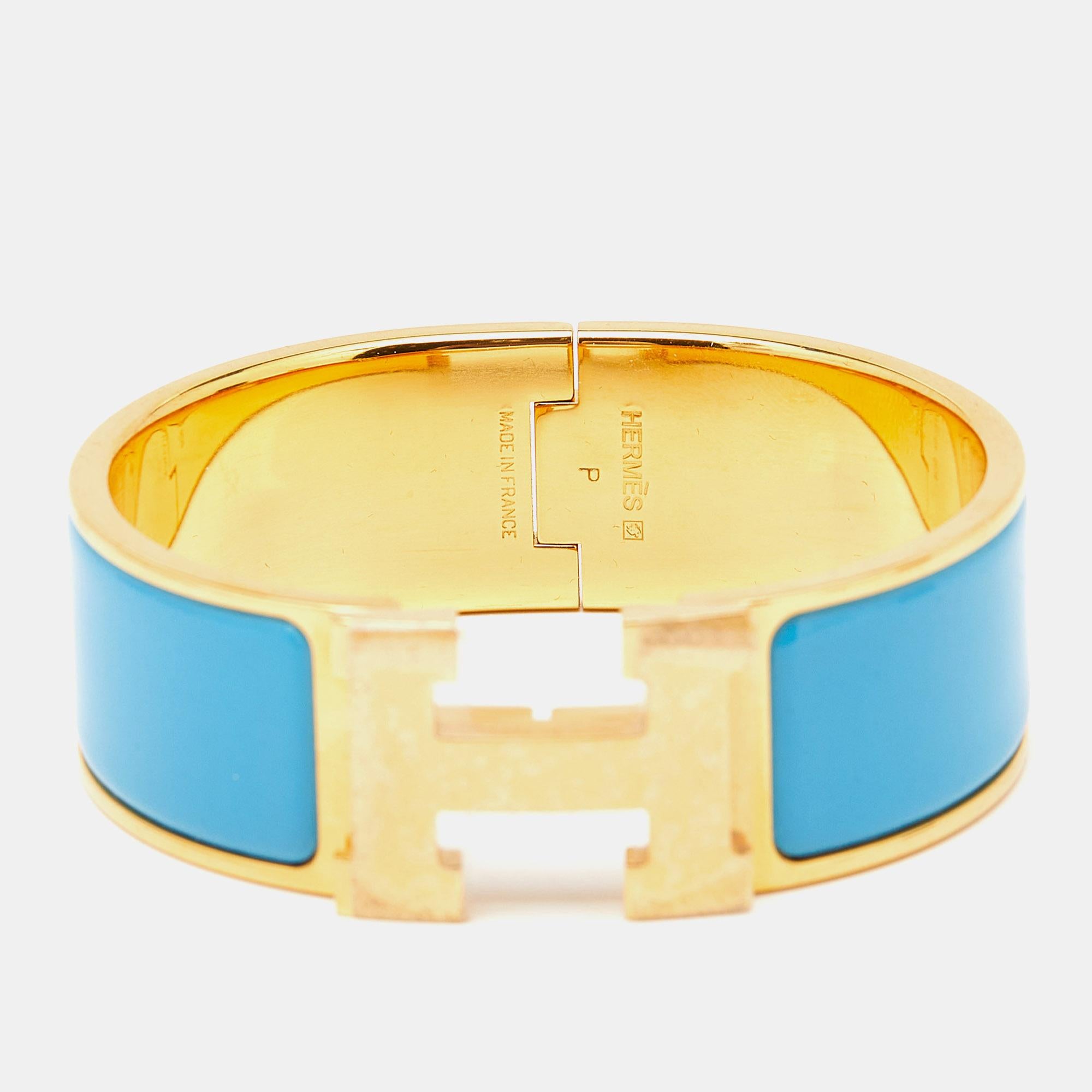 The Hermès Clic Clac H bracelet is an exquisite piece of jewelry. It features a glossy blue enamel band with a prominent gold-plated H-shaped clasp, creating a striking contrast. This luxurious and elegant accessory embodies timeless style and